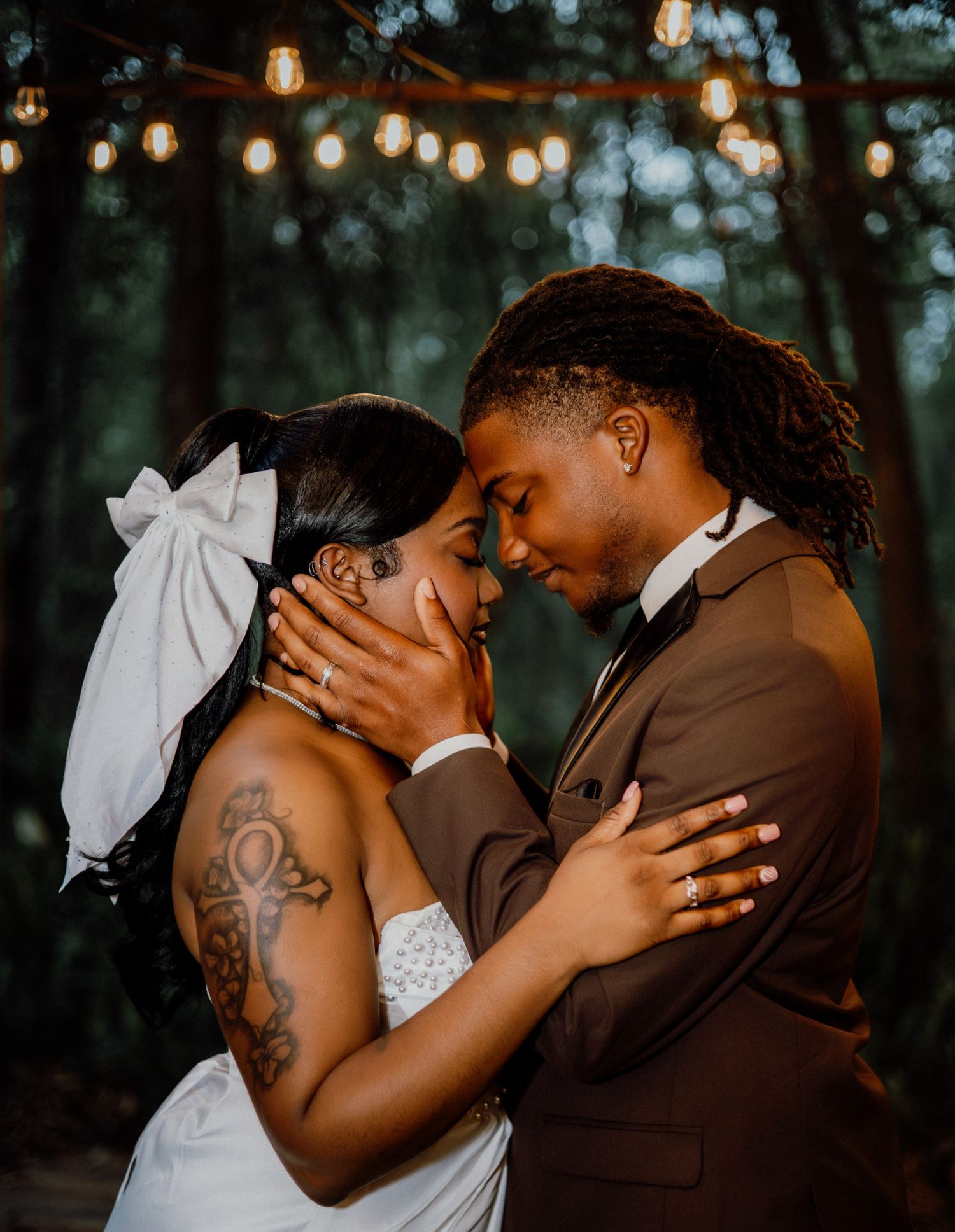 A romantic wedding couple embraces in an intimate moment under trees during golden hour lighting.