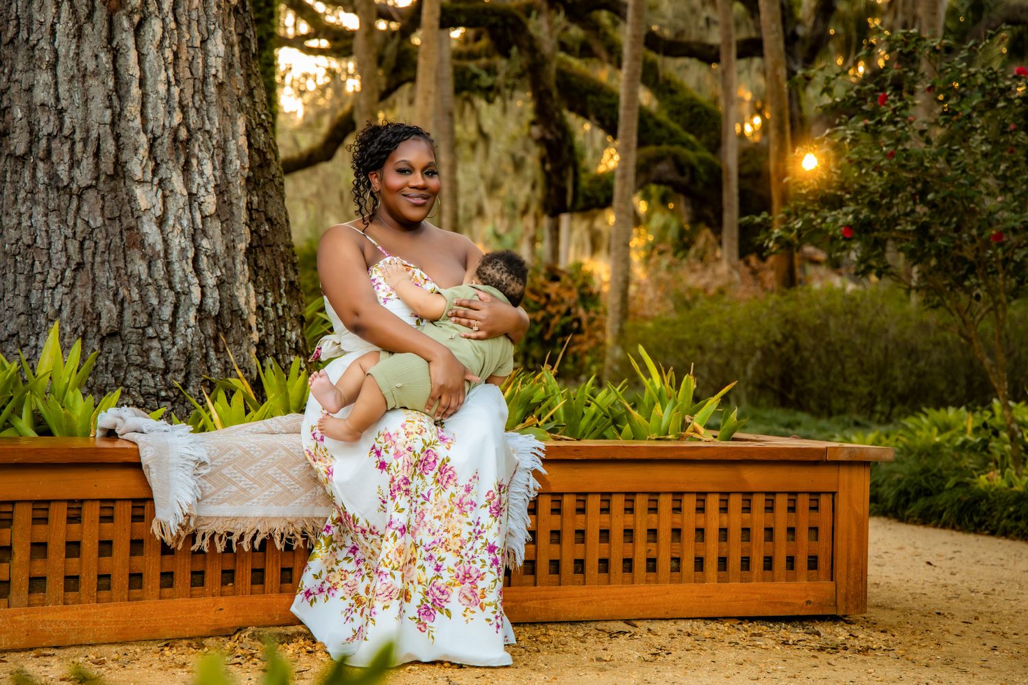 A person in a floral dress sits on a wooden bench in a lush garden setting at golden hour.