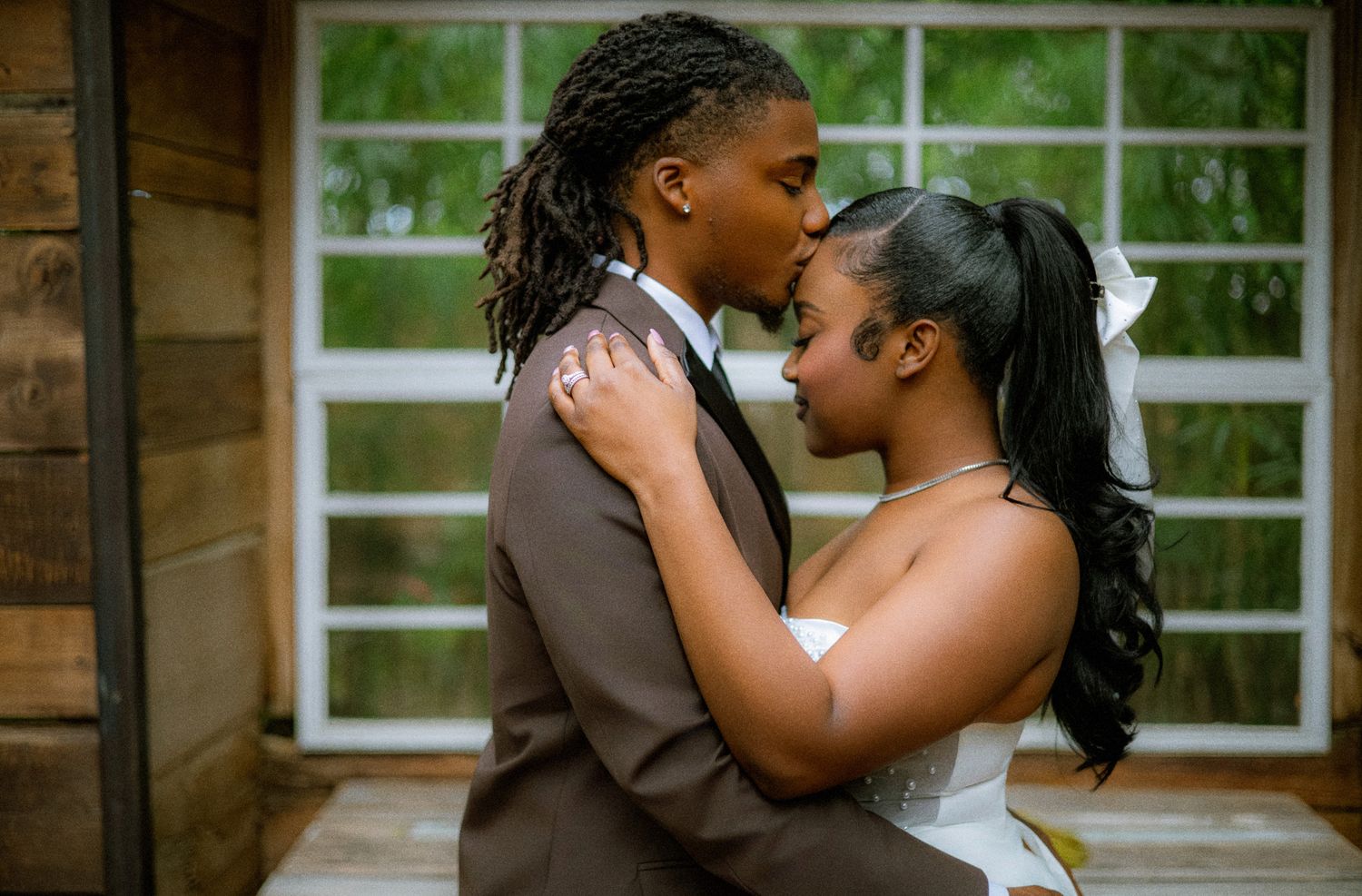A romantic couple shares a tender kiss during their wedding photoshoot in a rustic wooden cabin setting.