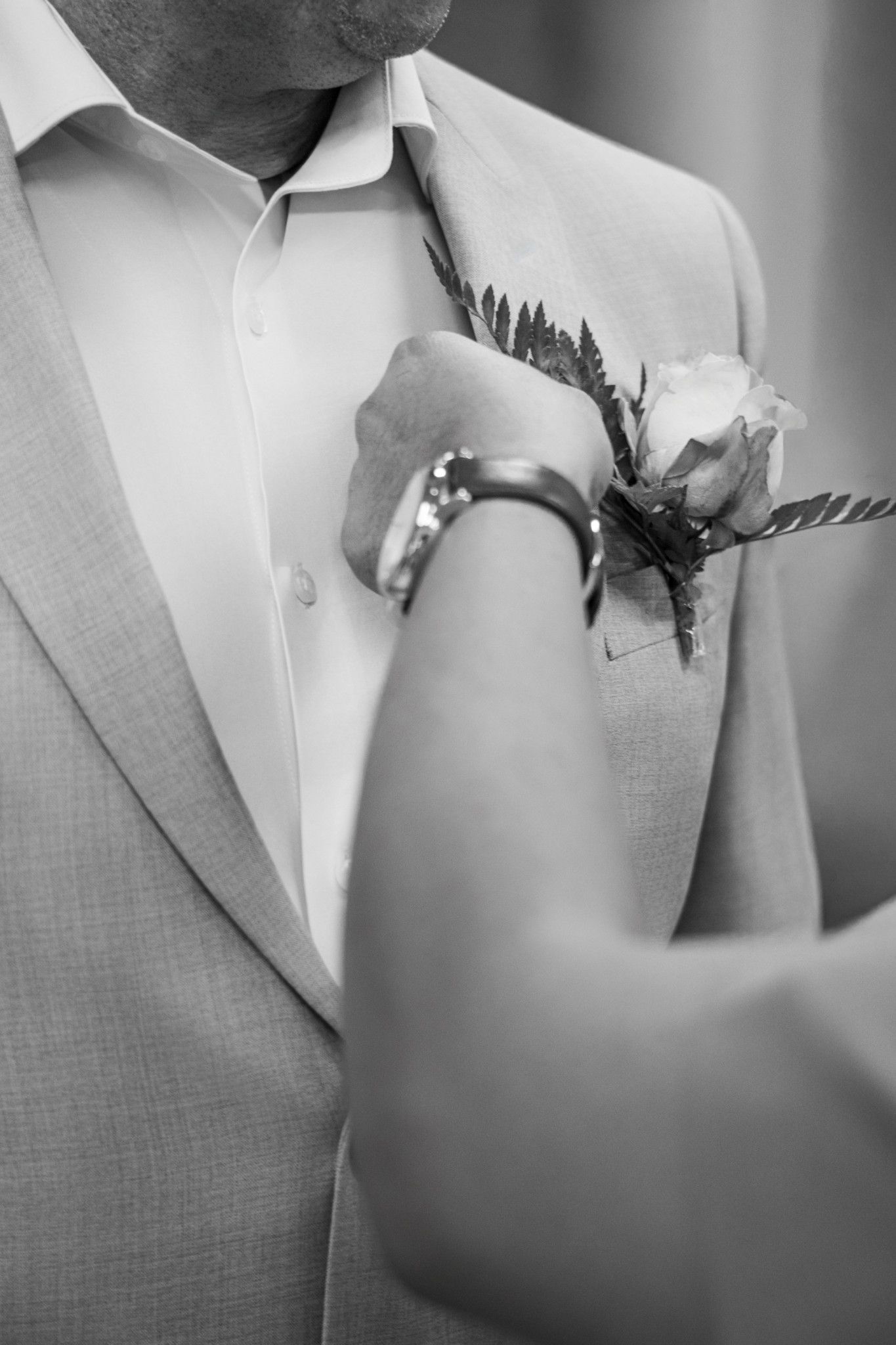 Black and white photo of a boutonniere being pinned onto a groom's lapel on his wedding day.