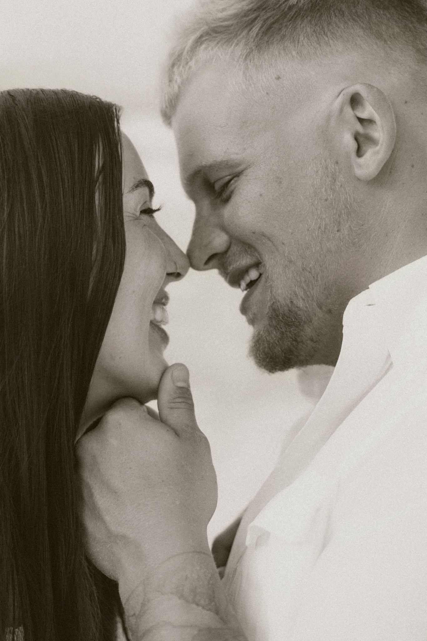 Black and white close-up of a smiling couple almost kissing, man gently holding womans chin.