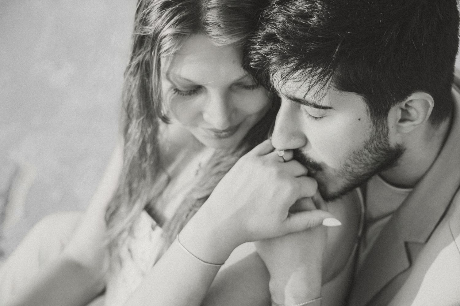 Black and white romantic photo of a couple, man gently kissing woman's hand in tender embrace.