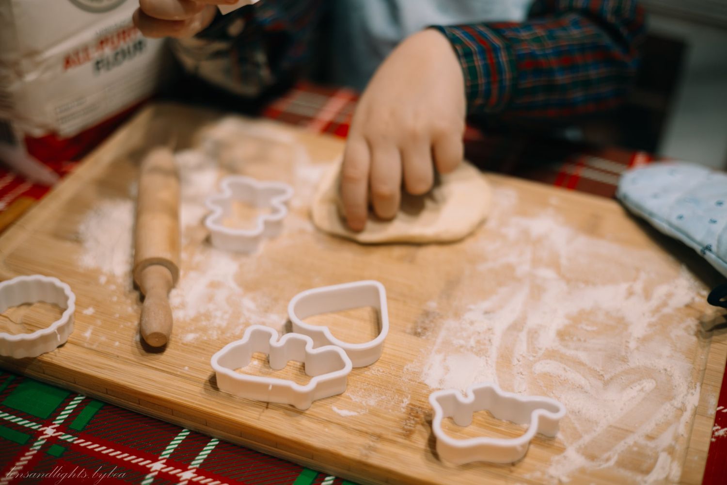 Rolling pin flattening dough on a wooden cutting board with cookie cutters and flour dusting.