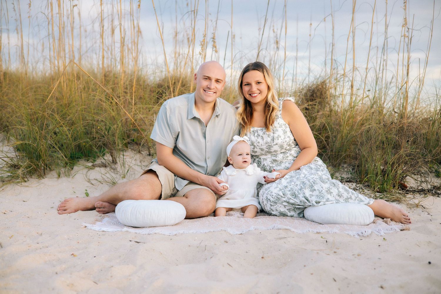 Family relaxing together on white sand beach with sea oats in background.