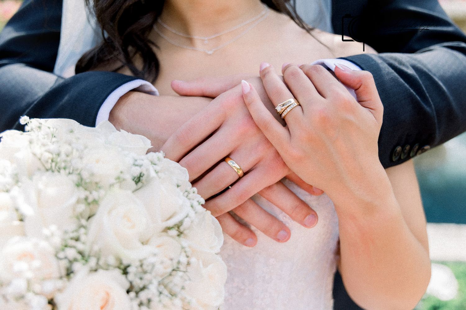 Close-up of bride and groom hands showing wedding rings with white bridal bouquet.