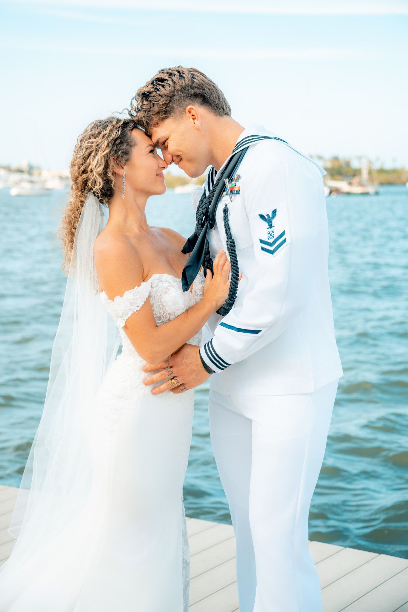 A bride and Navy sailor groom share a romantic moment on a waterfront dock on their wedding day.