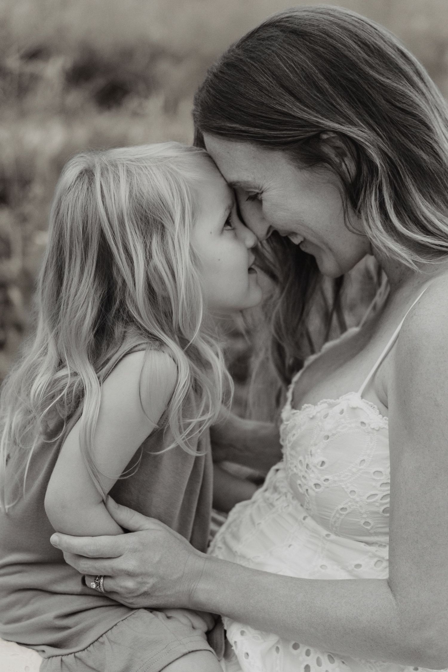 Black and white photo of a mother and young daughter touching foreheads and smiling in a tender moment.