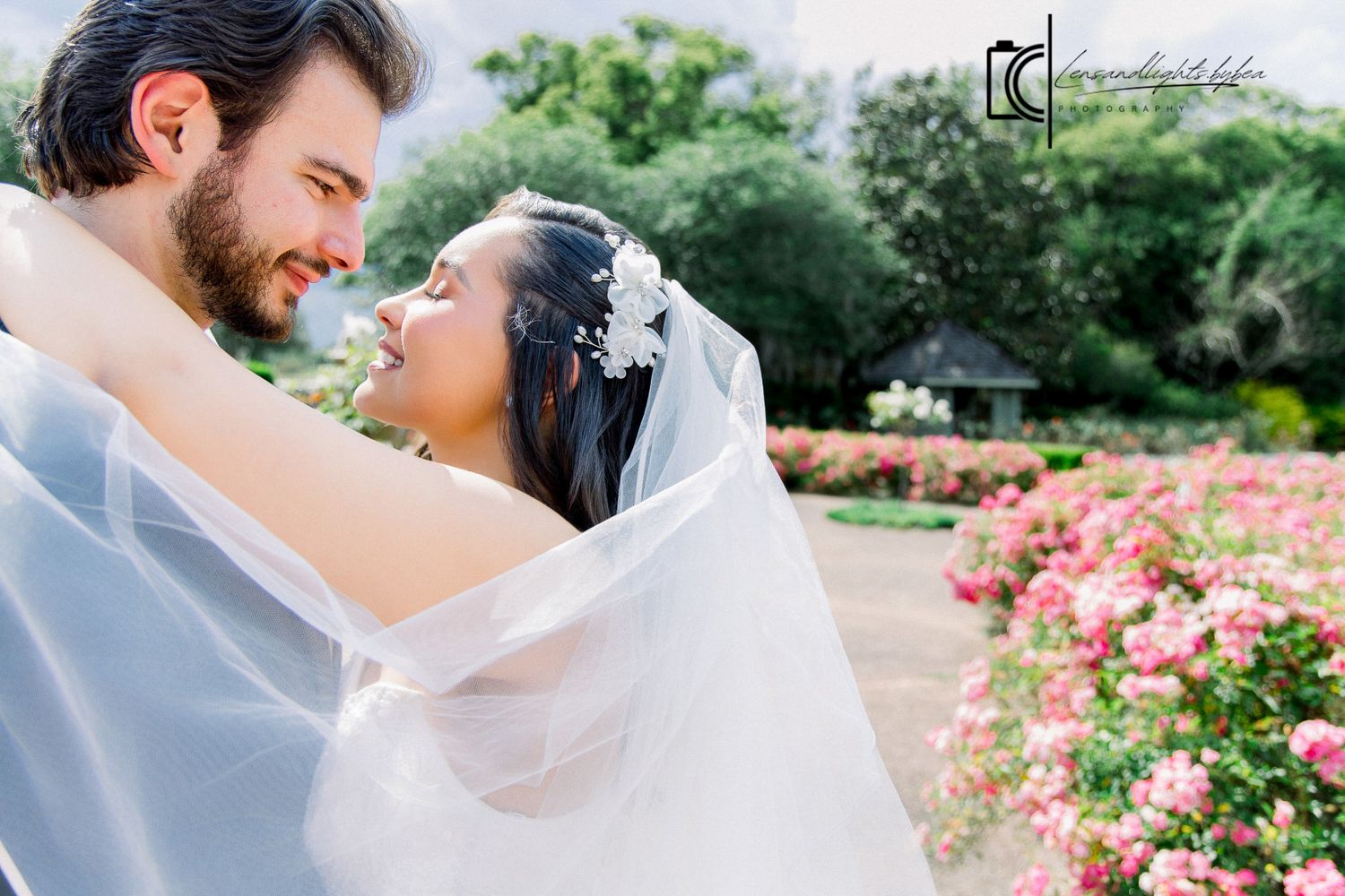 Smiling bride in veil embraced by groom in a romantic garden wedding photo.