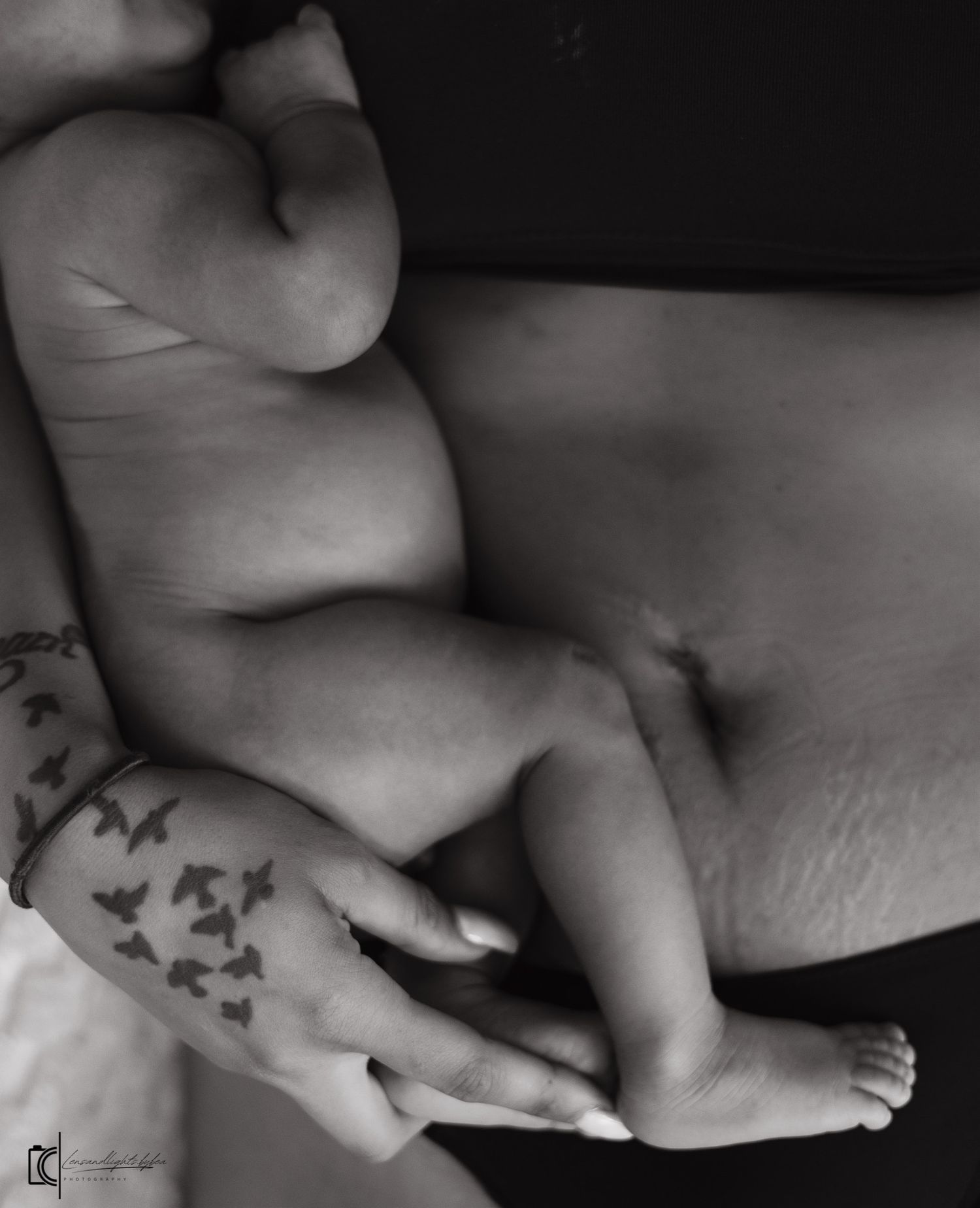 Black and white photo of a newborn baby cradled in a parent's tattooed hands against their torso.
