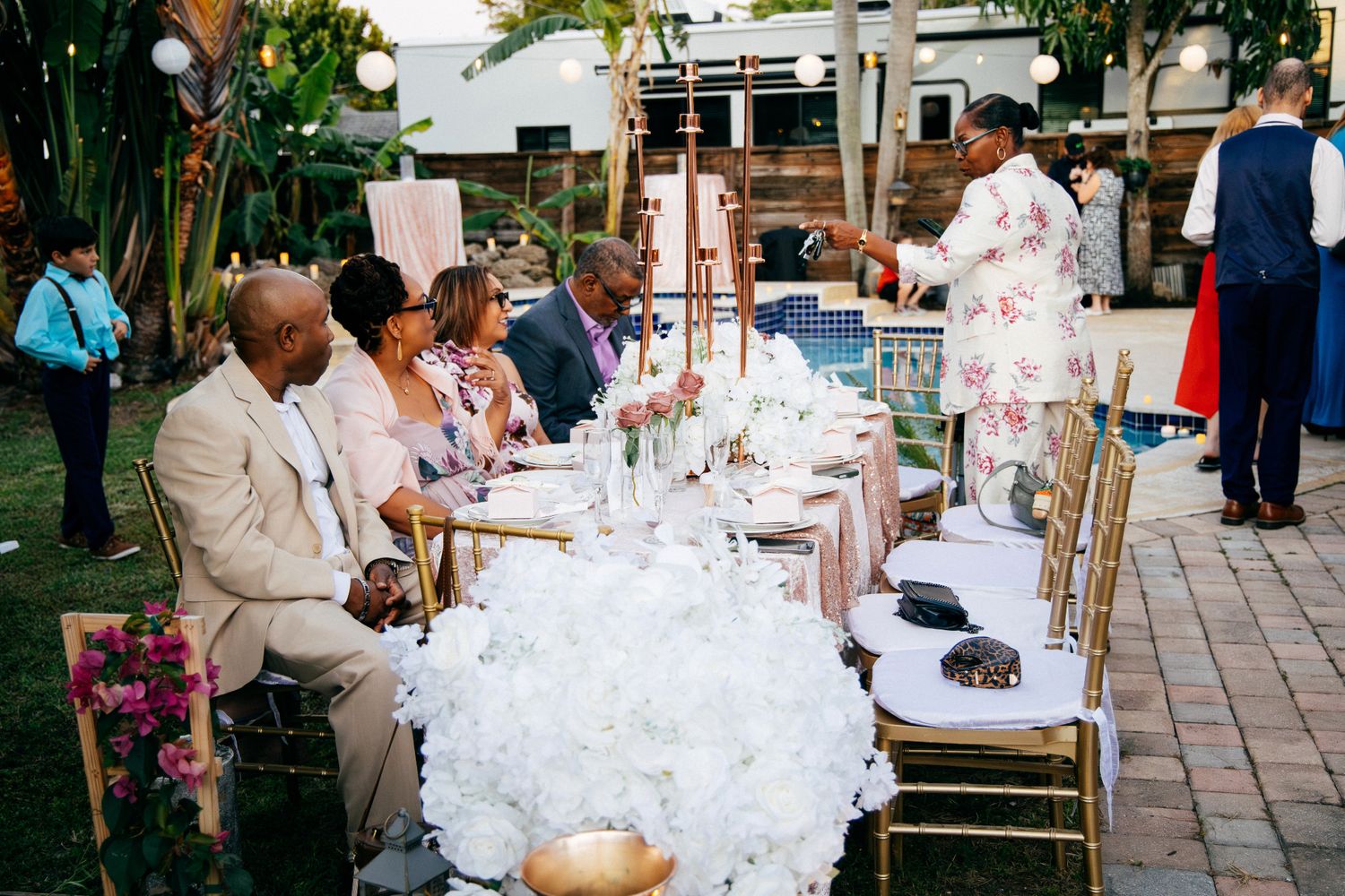 A group of people celebrate at an elegant outdoor wedding reception with white table settings and decor.