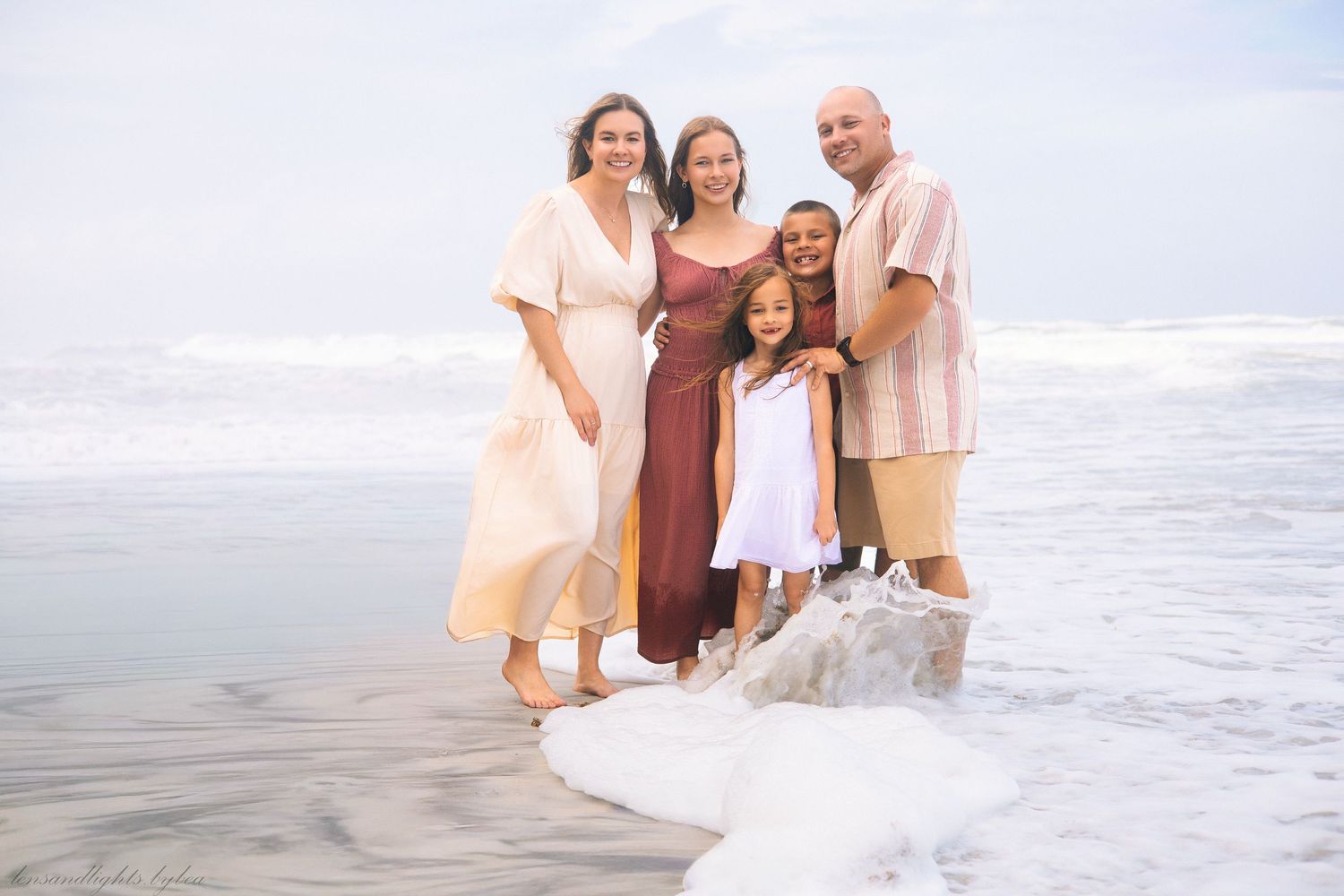 Family plays together in the ocean waves during a beach photoshoot.