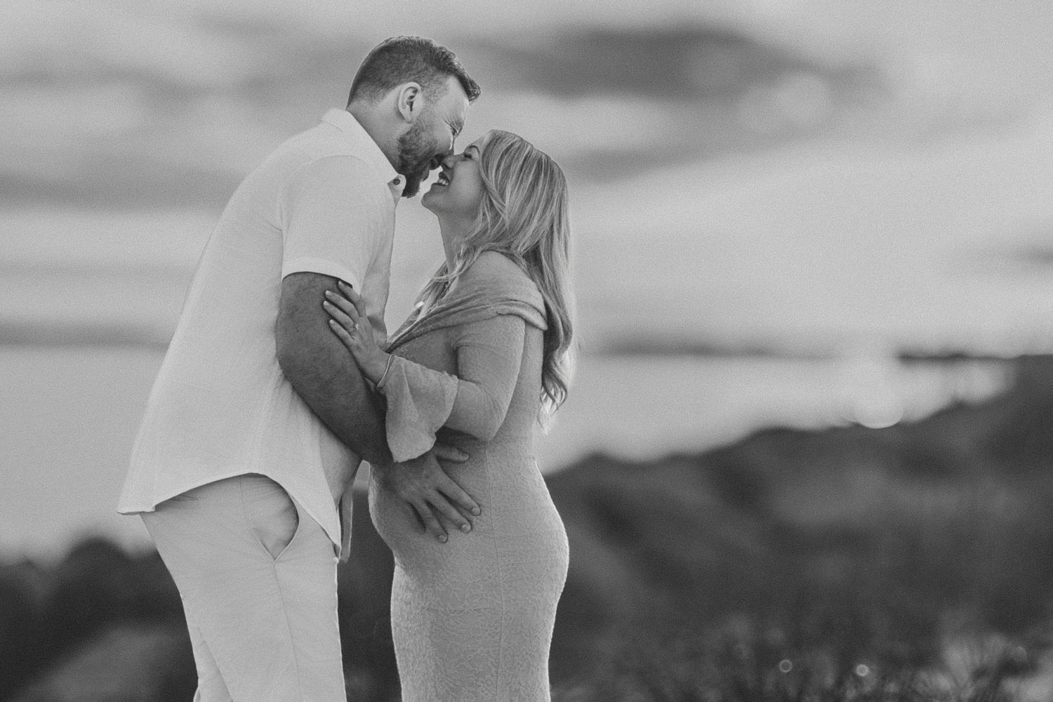 A romantic black and white photo series showing tender moments between a couple embracing on a beach at sunset.