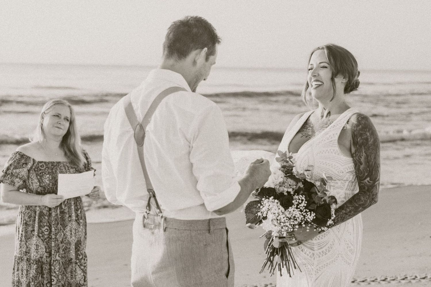 Bride and groom exchanging vows at a beach wedding ceremony in black and white photo.