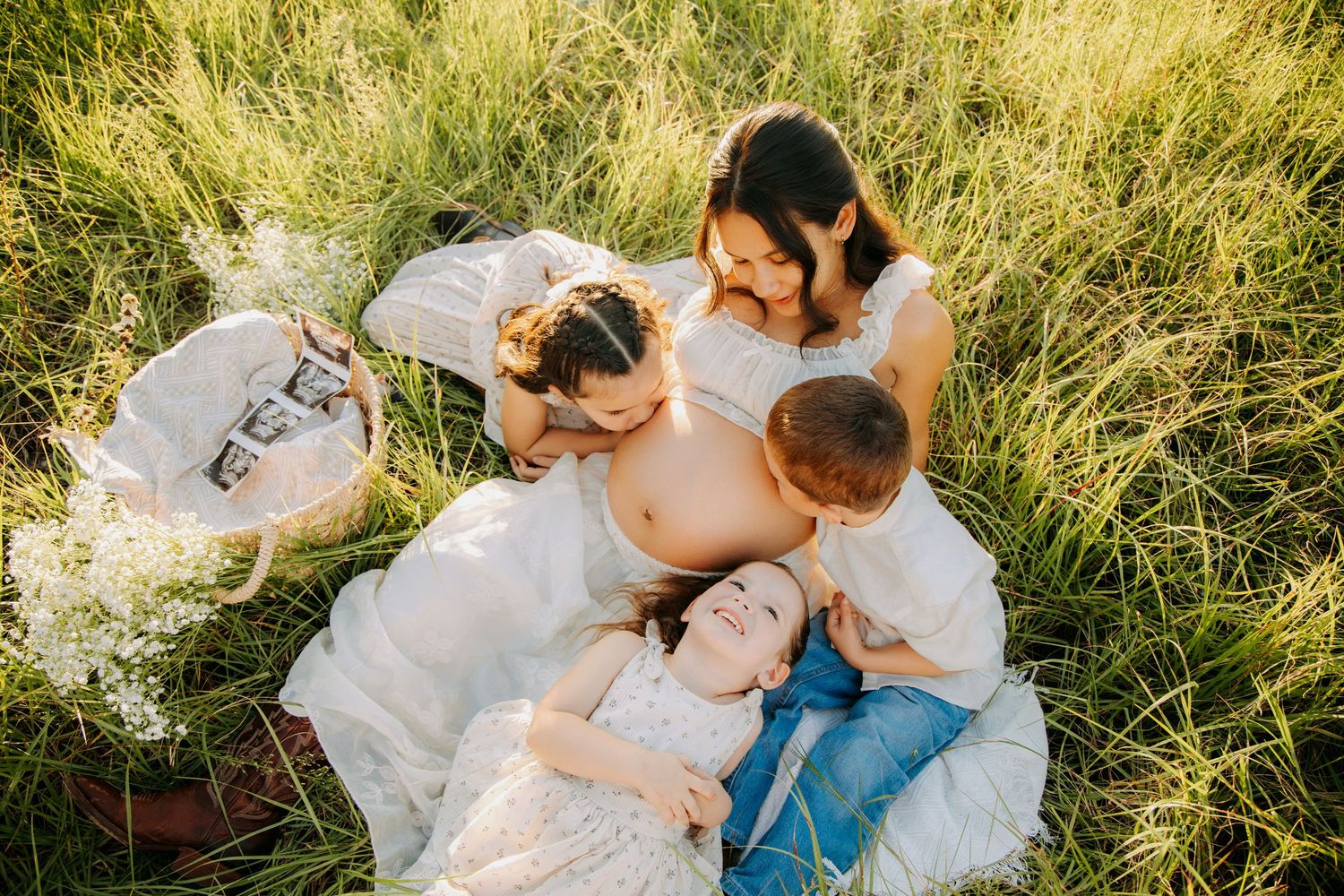 Pregnant woman with family sitting in green grass field during golden hour maternity photoshoot.