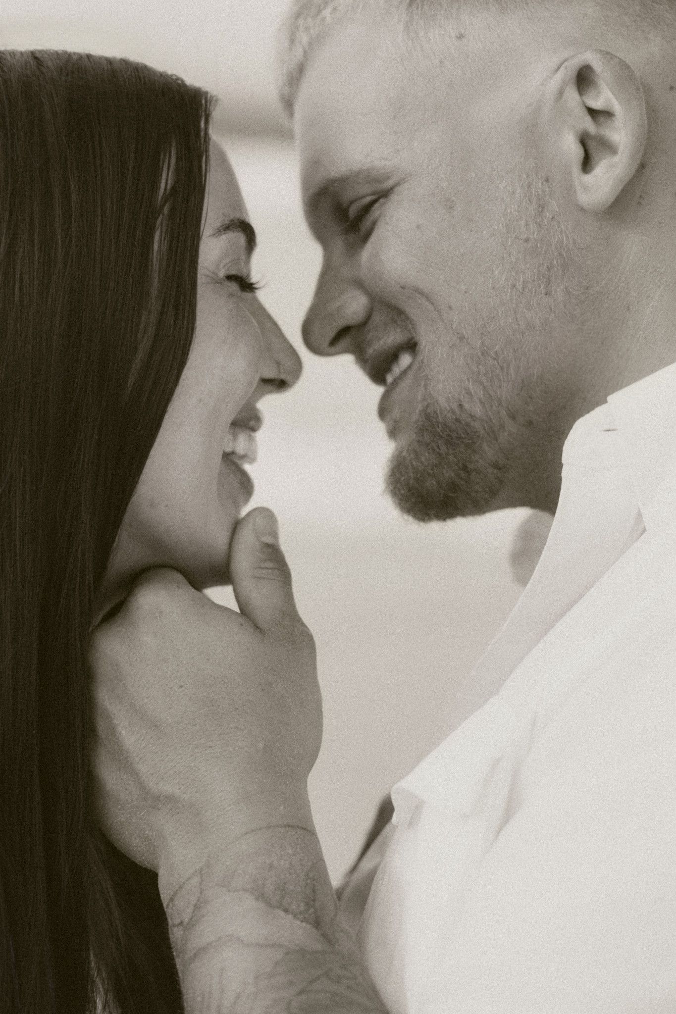 Black and white close-up of a smiling couple gazing at each other tenderly, man gently holding womans face.