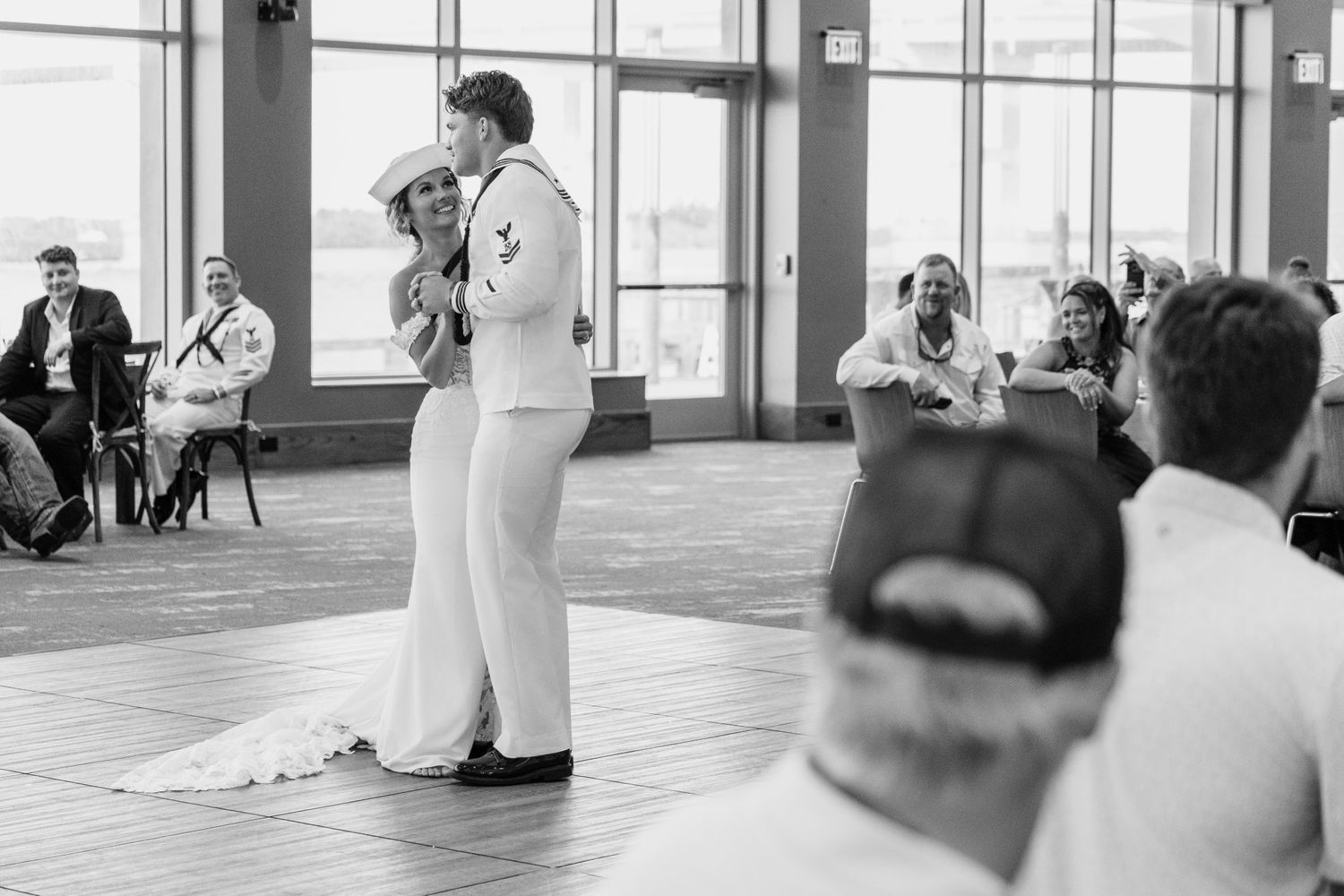 Navy sailor and bride share first dance at elegant indoor wedding reception in black and white photo.