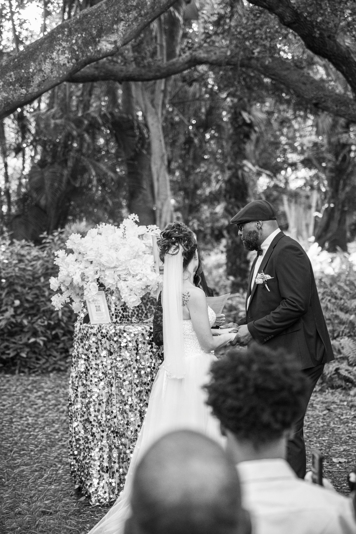 A black and white wedding photo sequence shows a couple in formal attire walking together under tree branches outdoors.