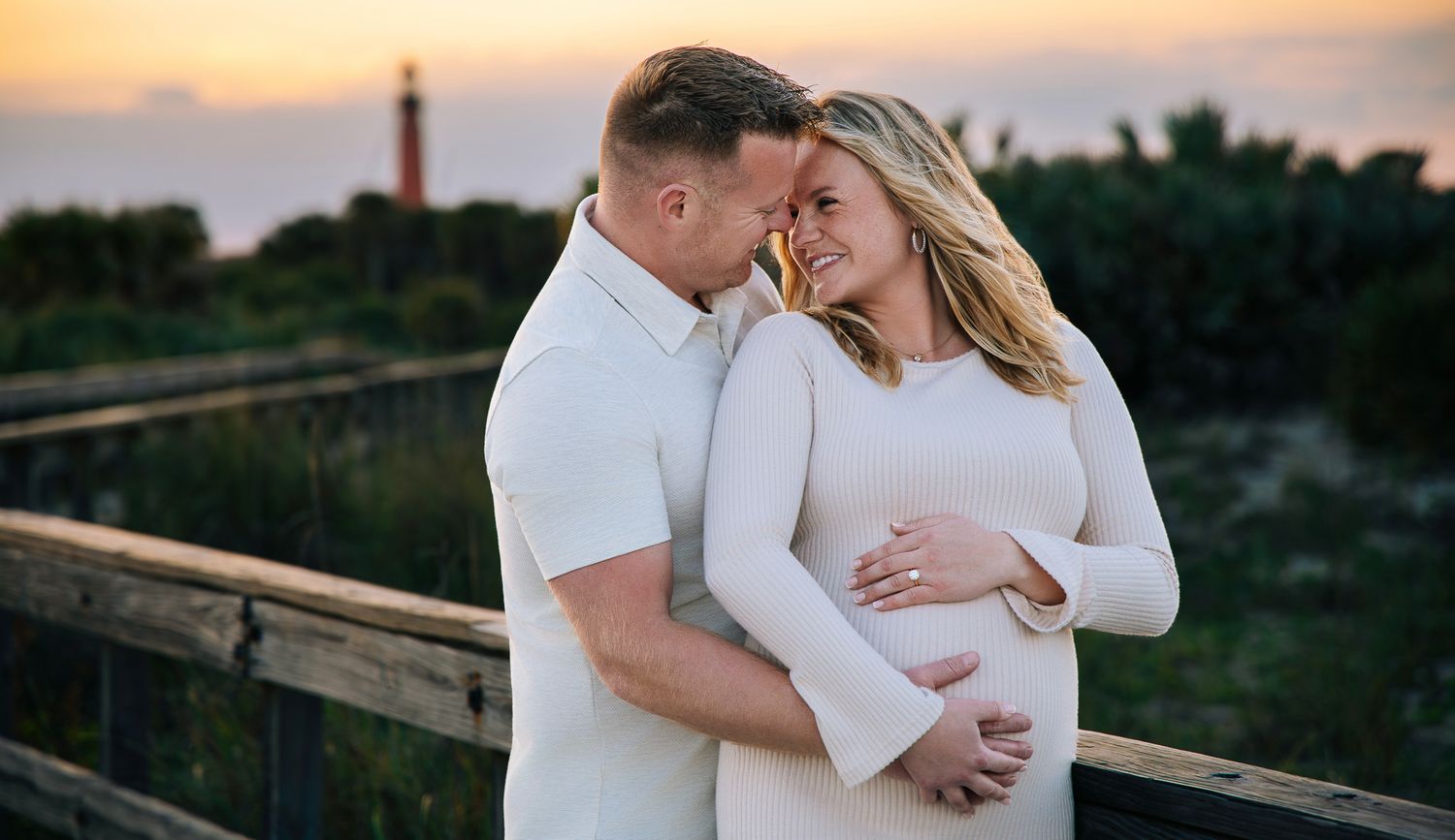 Couple in white outfits embracing during sunset photoshoot at outdoor location.
