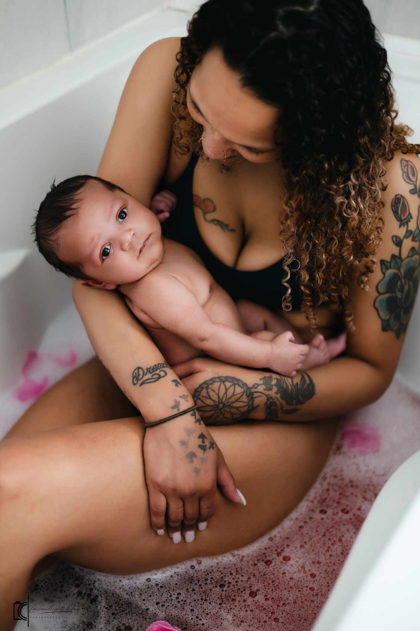 Intimate bathtub portrait showing tender moment between parent with tattoos and infant.