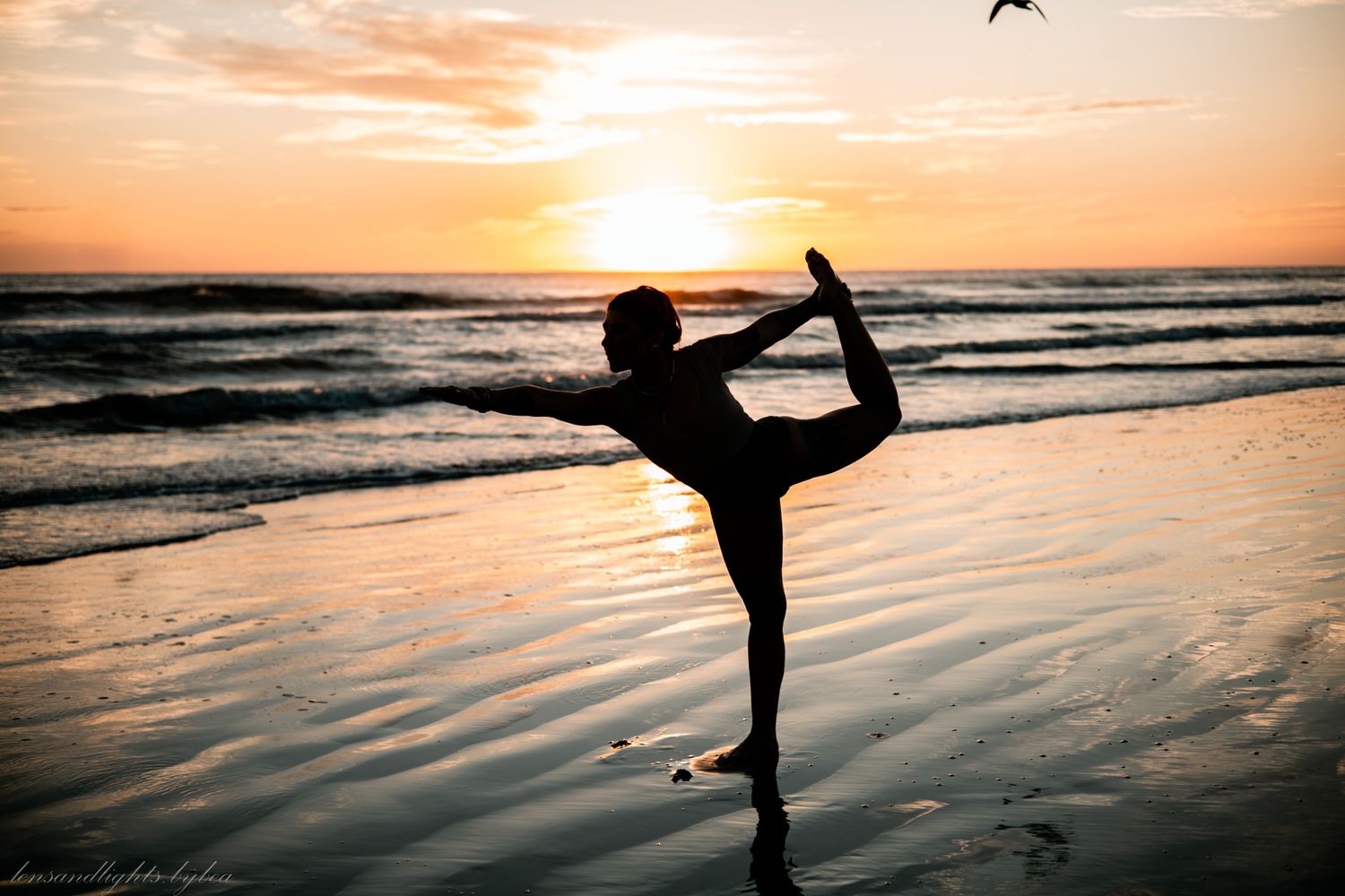 Silhouetted figure performs graceful dance poses against a vibrant orange sunset on the beach.