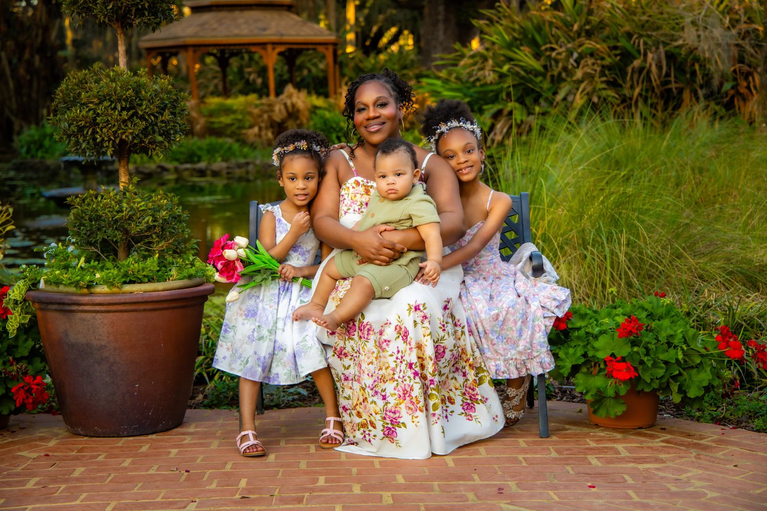 A group in floral dresses poses together in a lush garden setting with red flowers and greenery.