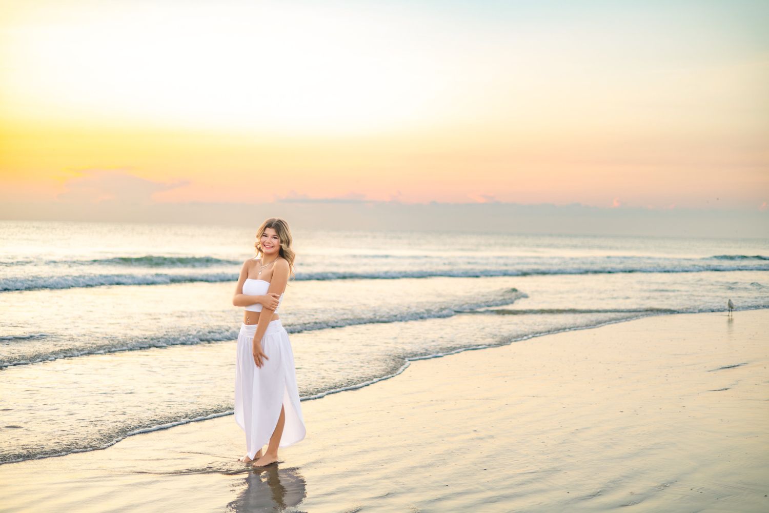 Woman in white dress walking on a sandy beach at sunset with golden sky and ocean waves.