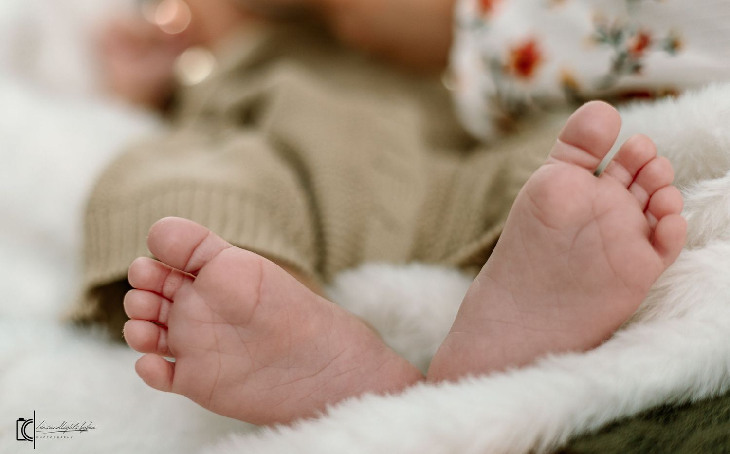 Tiny baby feet resting on soft white blanket with pink and red flowers in the background.