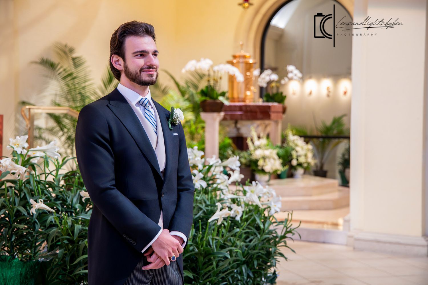 Handsome groom in dark suit and blue tie stands at flower-adorned church altar awaiting his bride.