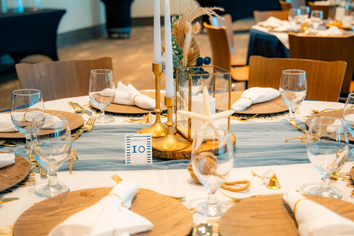 Elegant beach-themed wedding reception table with gold candlesticks, blue runner, starfish, and crystal glassware.