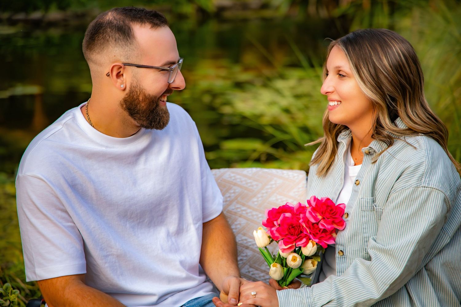 A couple in casual attire share joyful moments together in a garden setting with bright pink flowers.