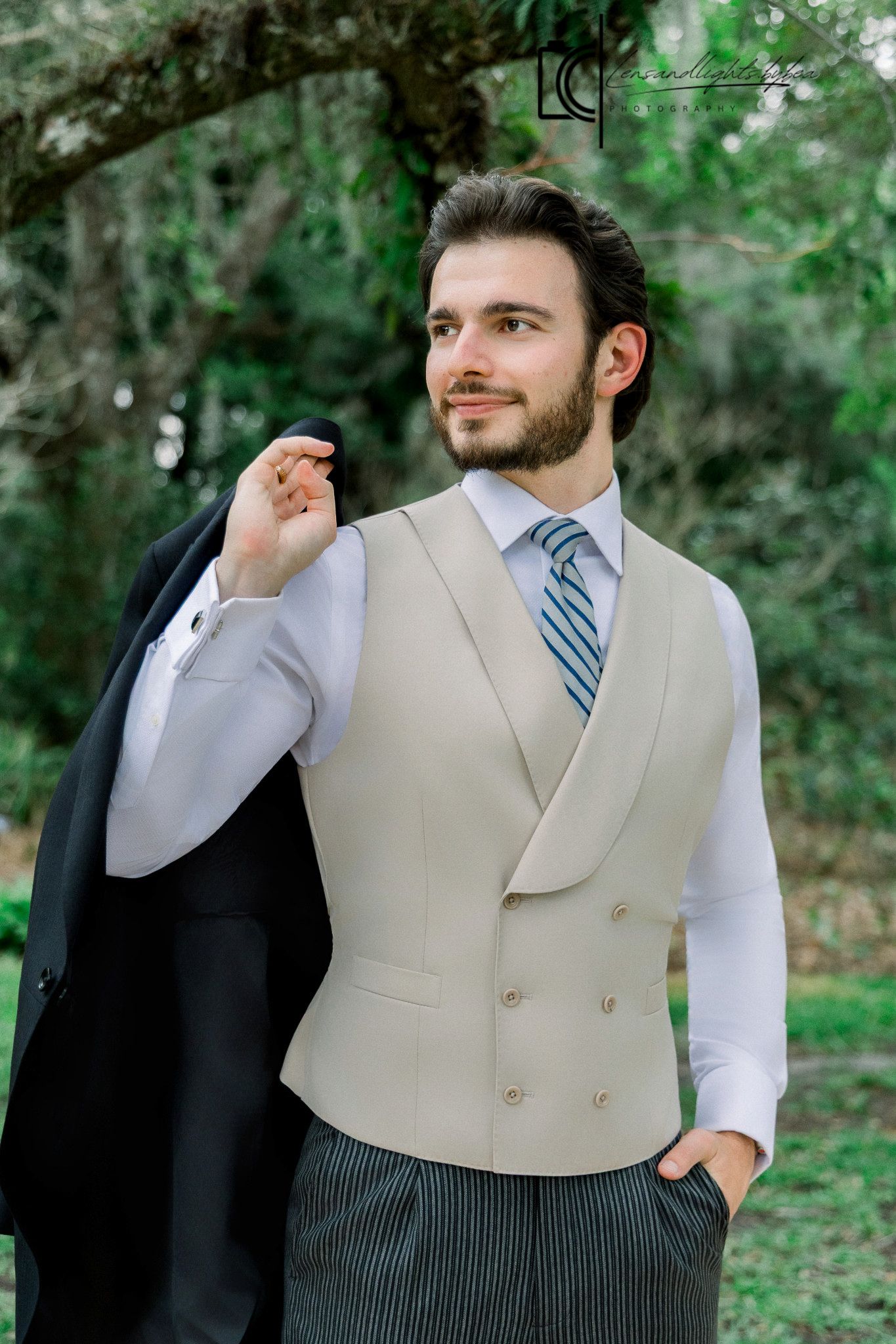 Dapper groom in beige double-breasted vest and striped tie holding suit jacket outdoors.