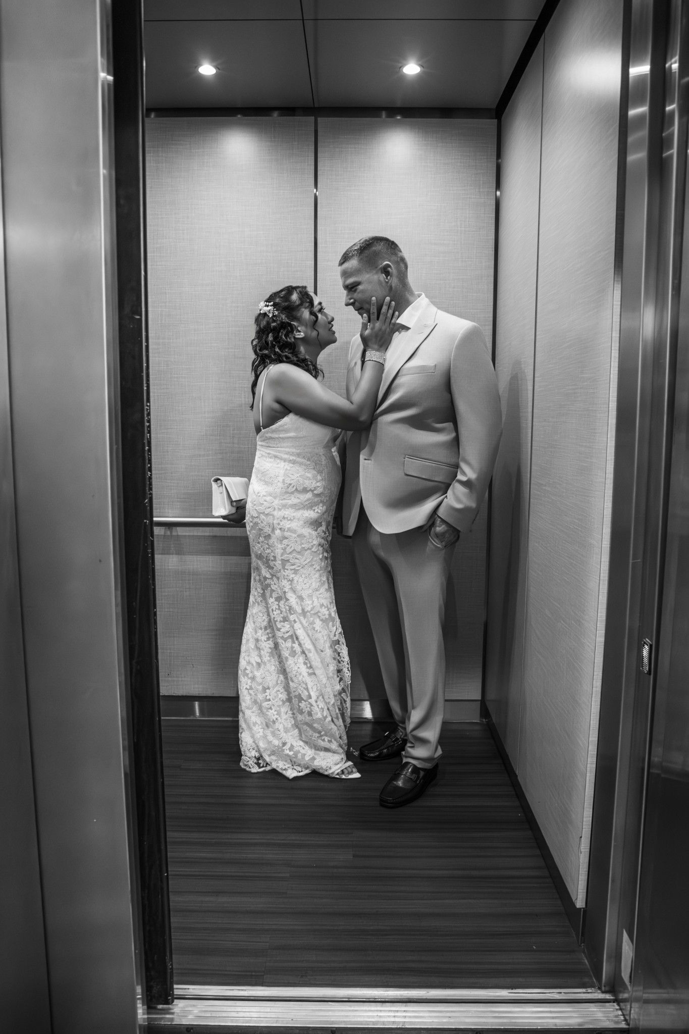 Black and white photo of a bride and groom sharing a romantic moment in an elevator on their wedding day.