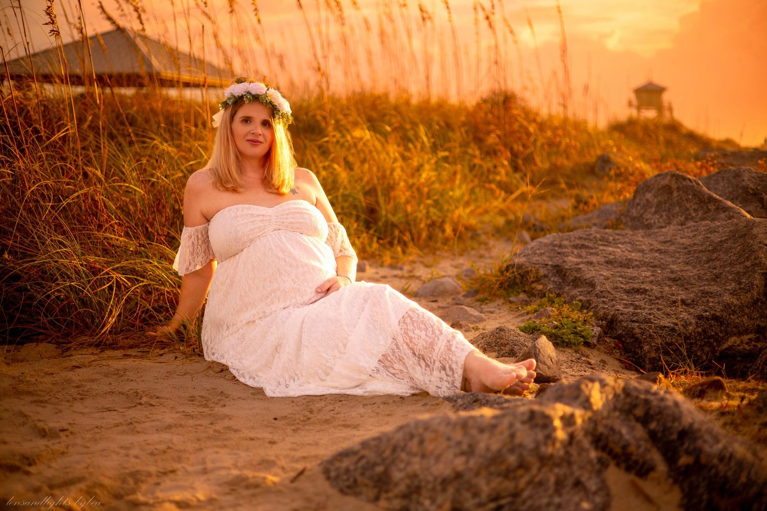 A person in white dress sits among beach rocks during golden hour.