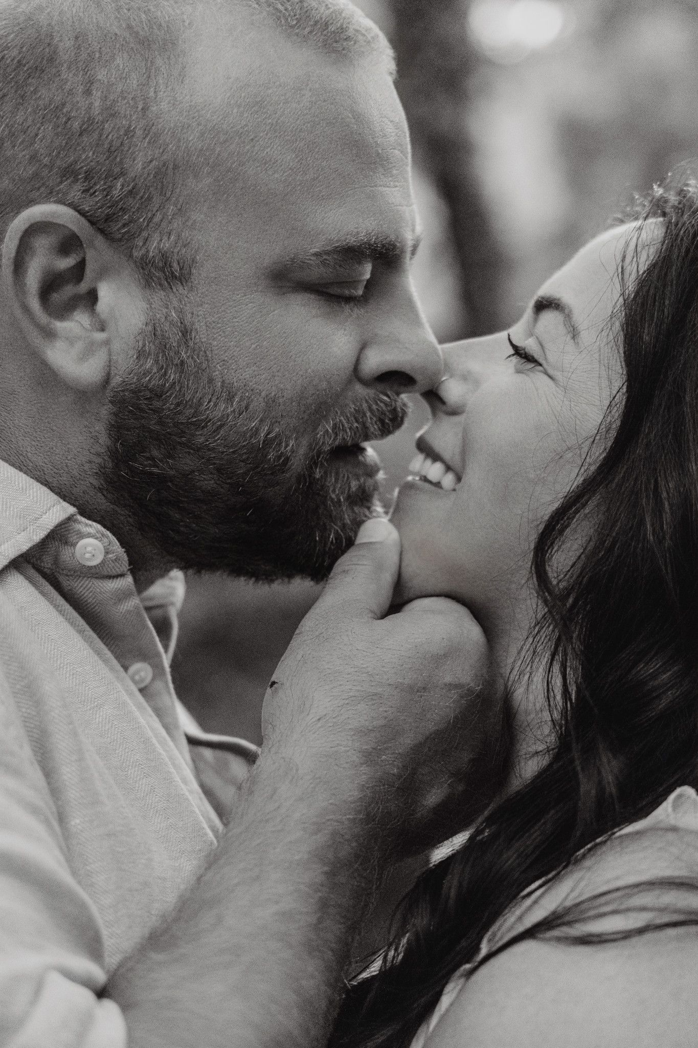 Black and white photo of a couple sharing a tender romantic moment, man gently holding woman's chin as she smiles.