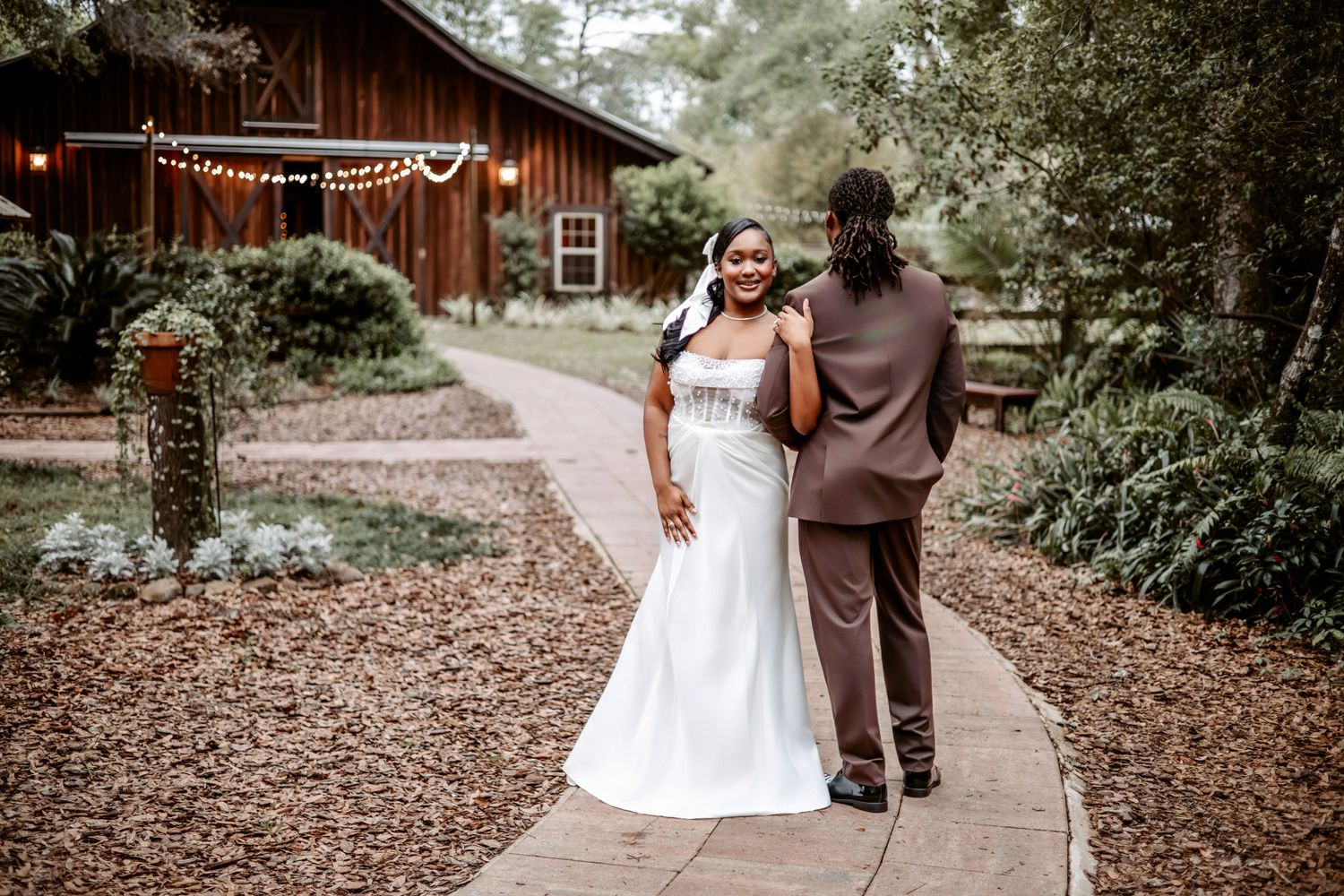 Couple walking hand in hand through a rustic outdoor venue decorated with string lights and natural foliage.
