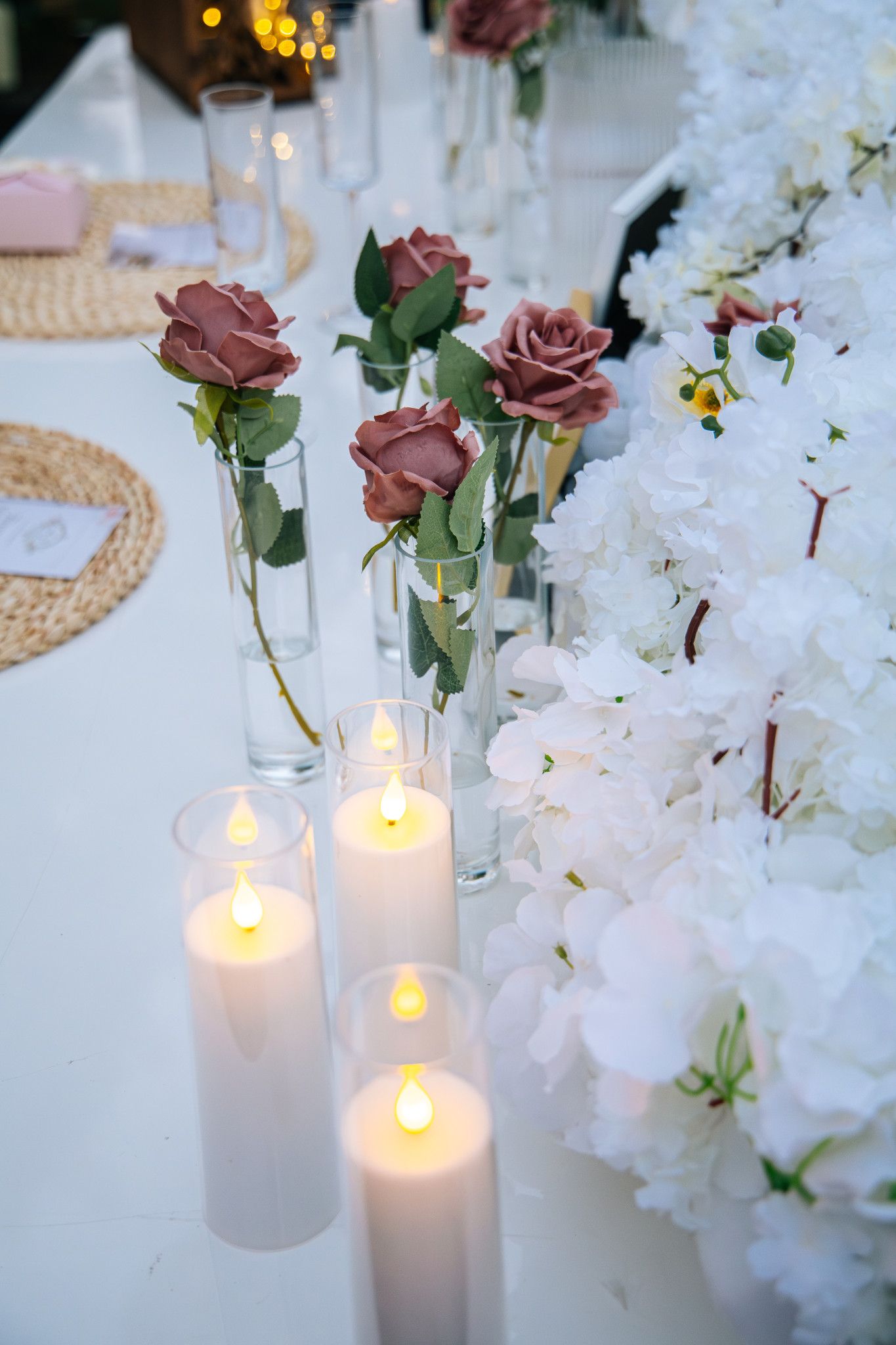 Elegant wedding table decor with mauve roses in glass vases, glowing white candles and delicate white orchids.