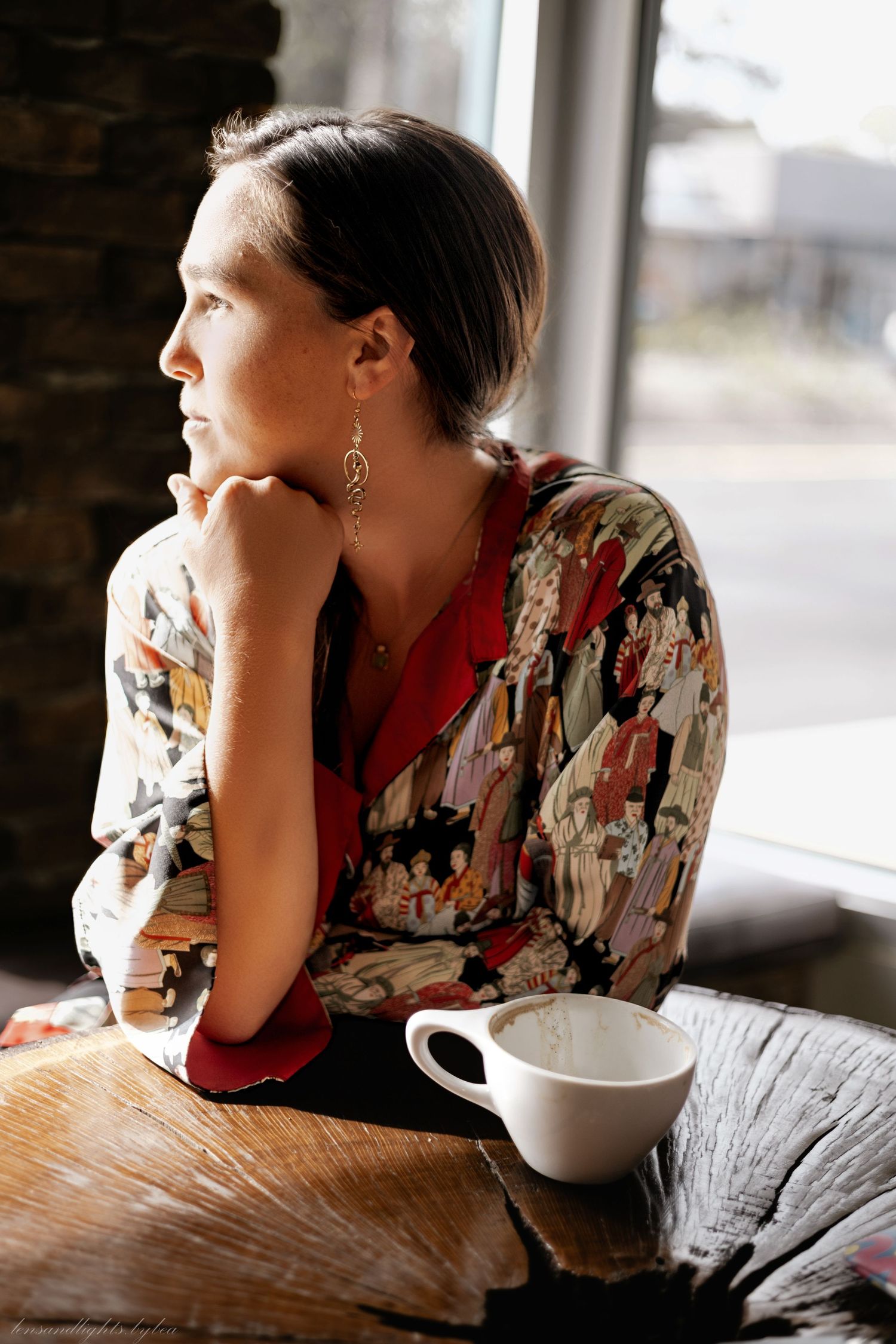 Person in floral print dress relaxing at cafe table with coffee cup.