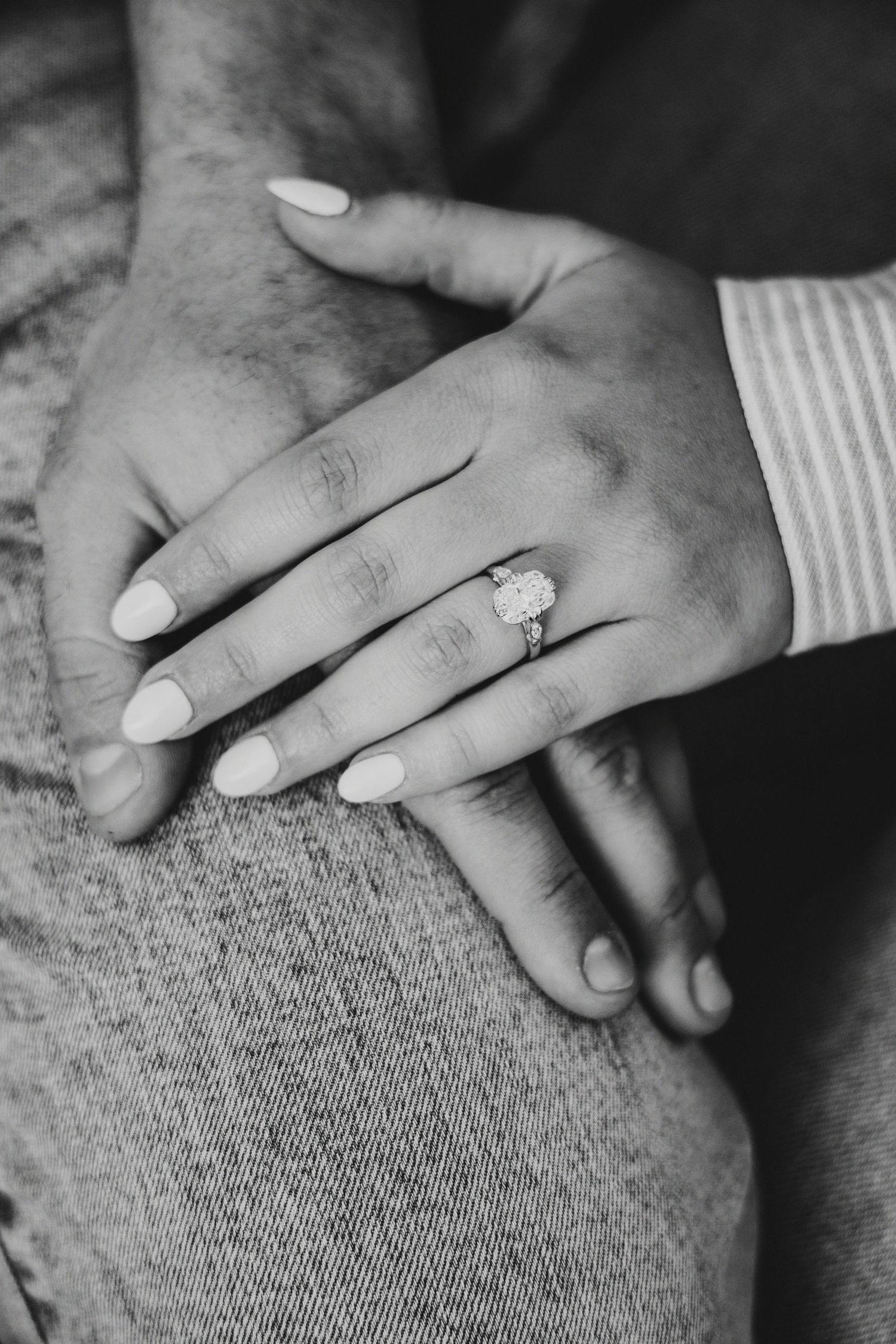 Black and white close-up of hands with an engagement ring resting on textured fabric.