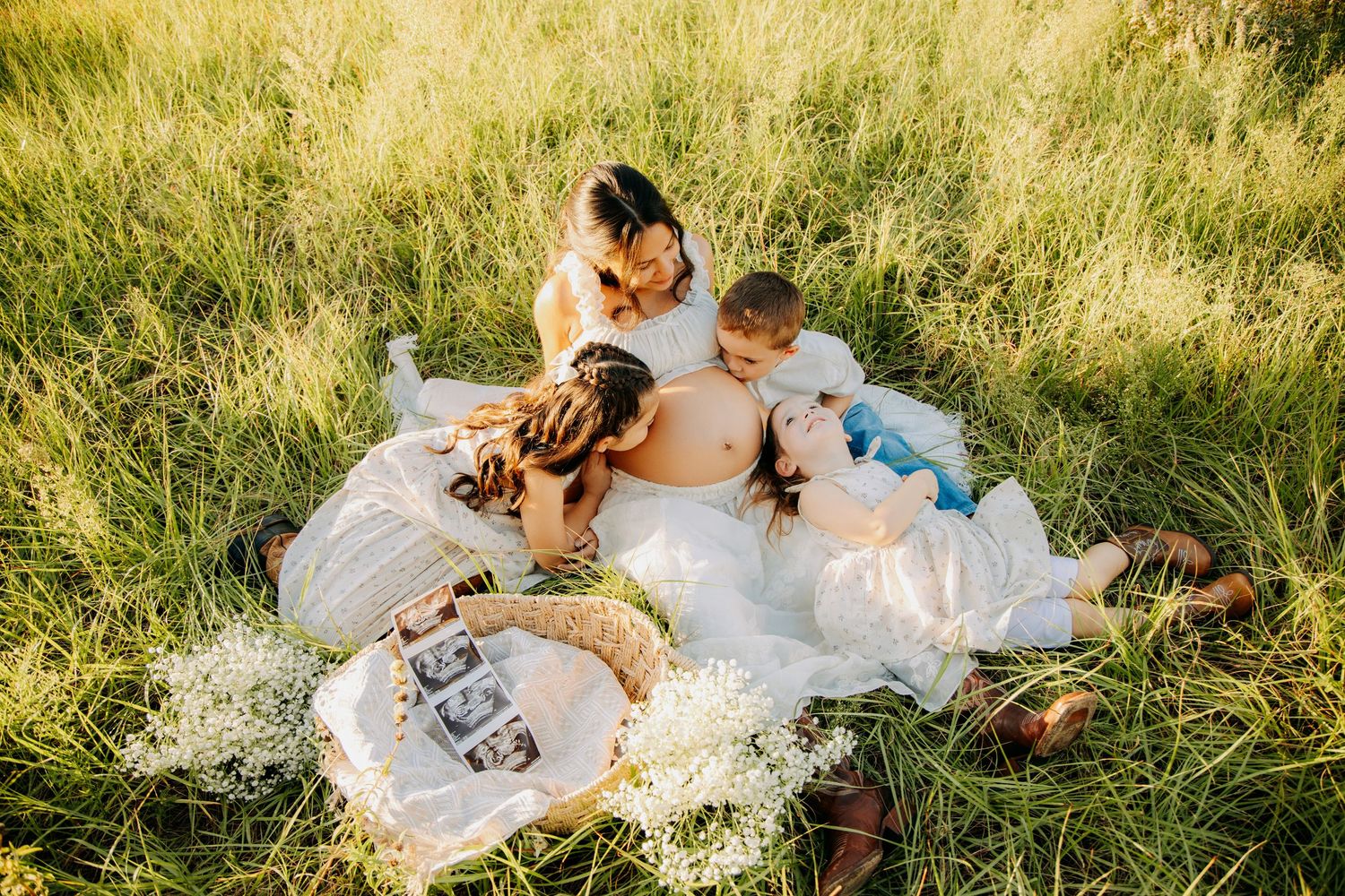 Aerial view of pregnant mother lying in field with family gathered around her, ultrasound photos displayed nearby.