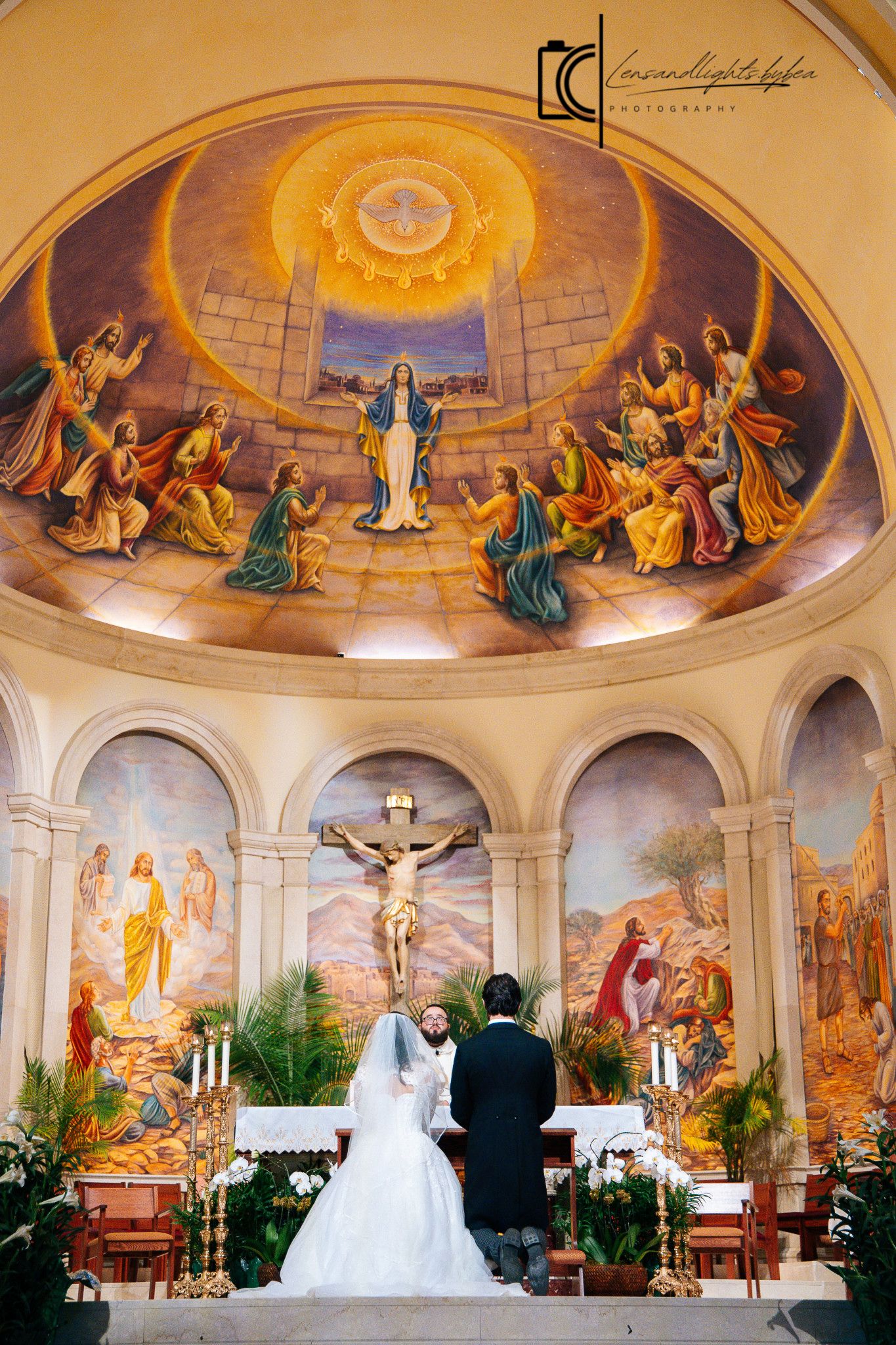 Bride and groom at the altar beneath a stunning domed fresco depicting Pentecost in a Catholic church.