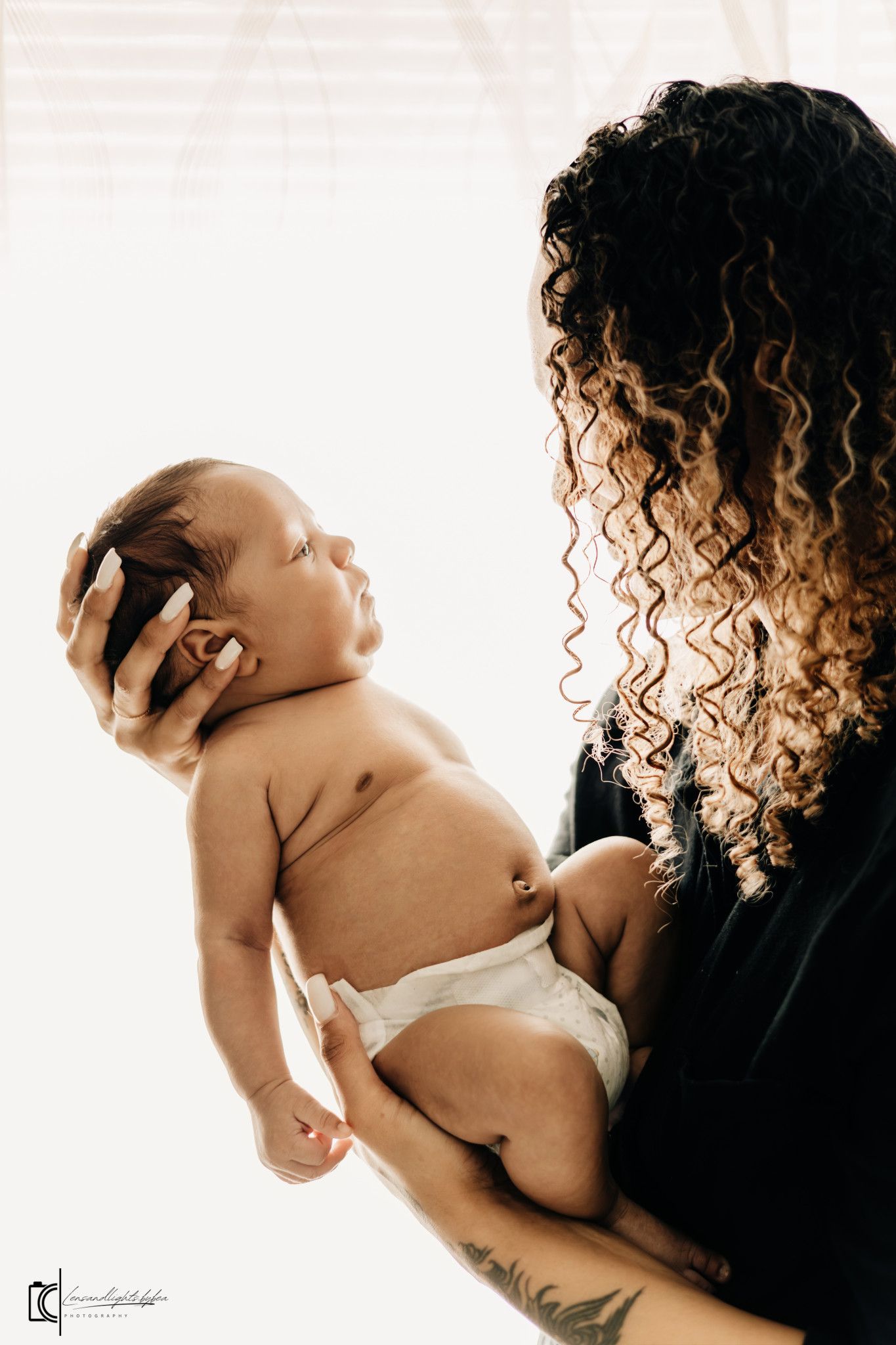 A tender moment between a caregiver with curly hair and a newborn baby wearing a diaper.