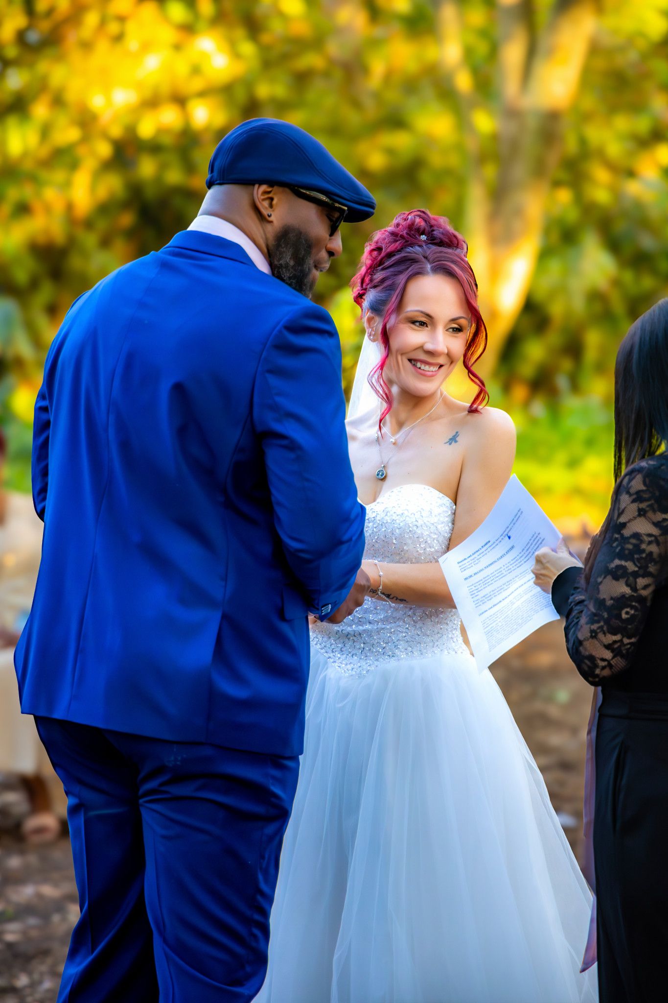 A couple shares a joyful moment during their outdoor wedding ceremony with autumn foliage in the background.