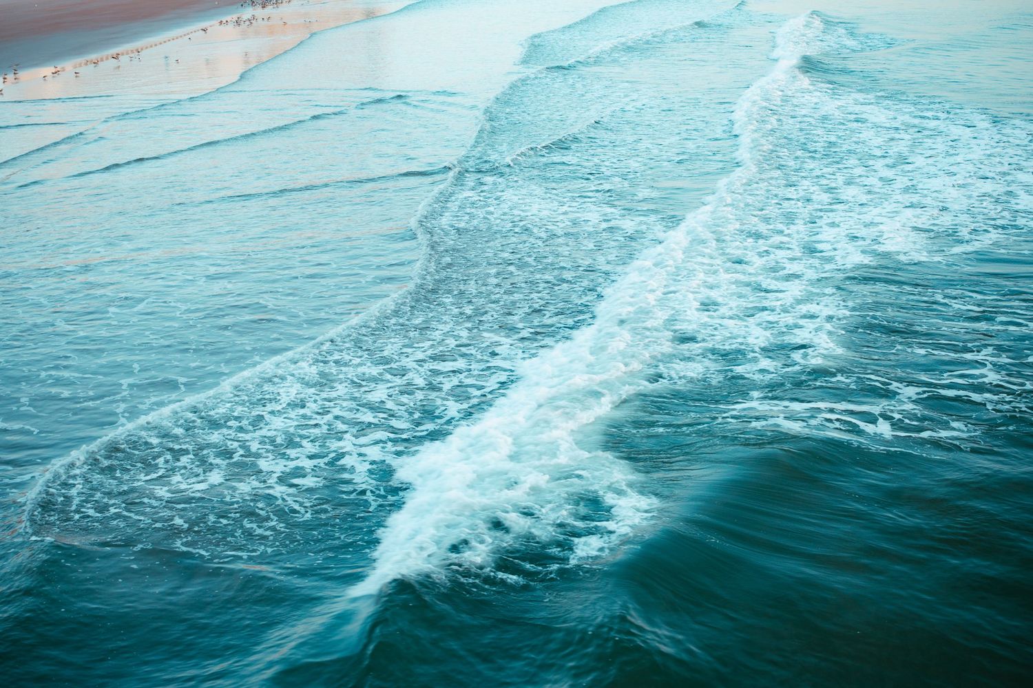 Aerial view of turquoise ocean waves creating white foam patterns along the water's surface.