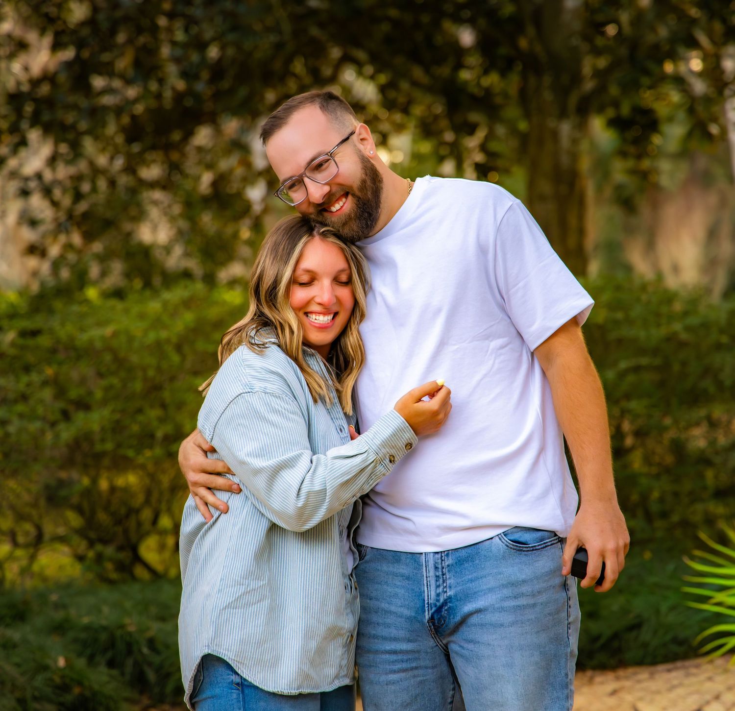 Couple embracing and laughing together during an outdoor photoshoot in a natural setting.