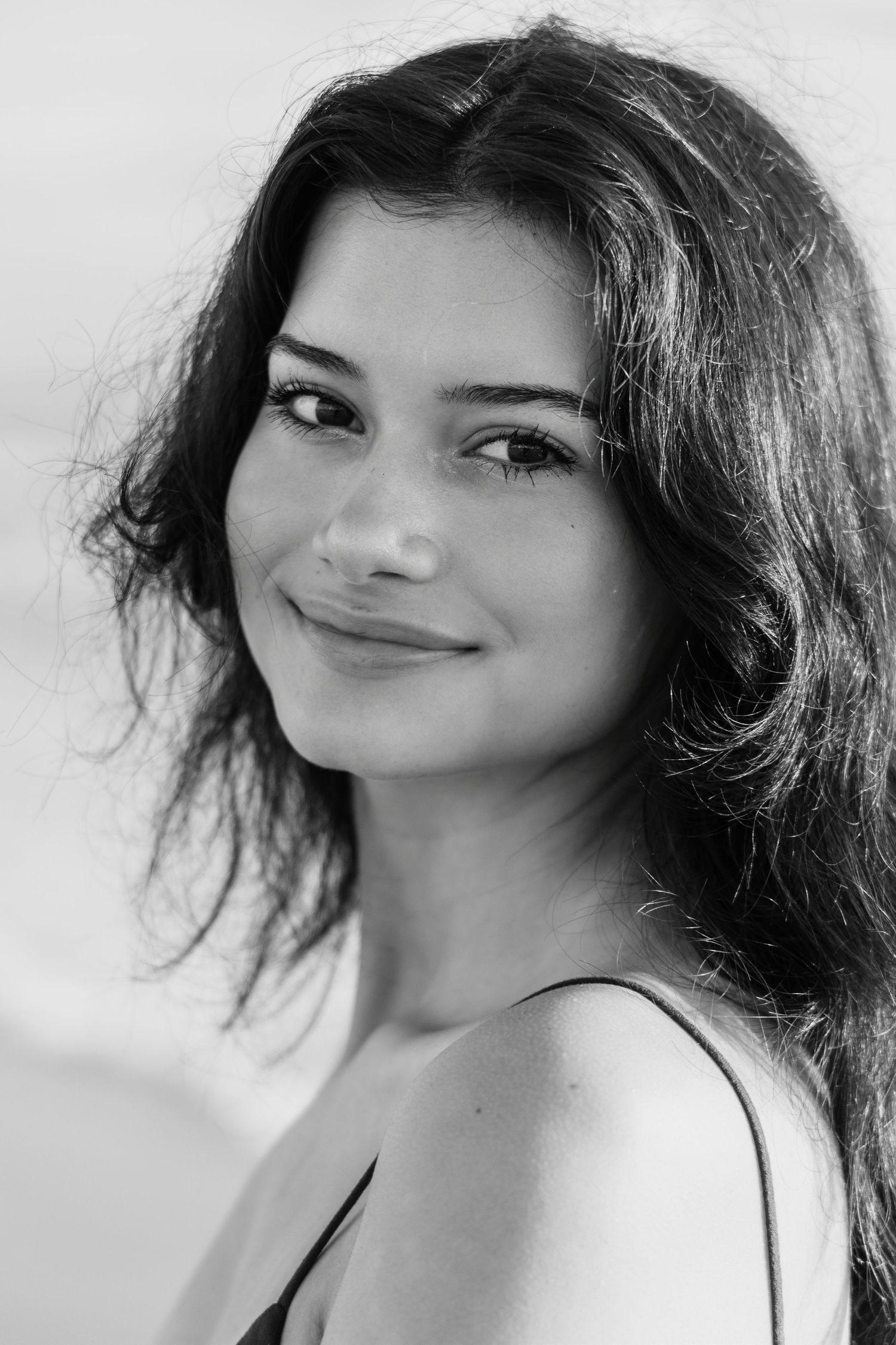 Black and white portrait of a young woman with dark wavy hair smiling softly at the camera outdoors.