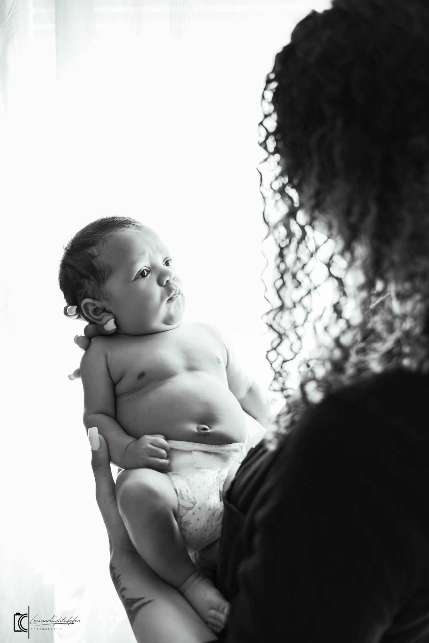 Black and white portrait of a small infant in a diaper looking up with curiosity.