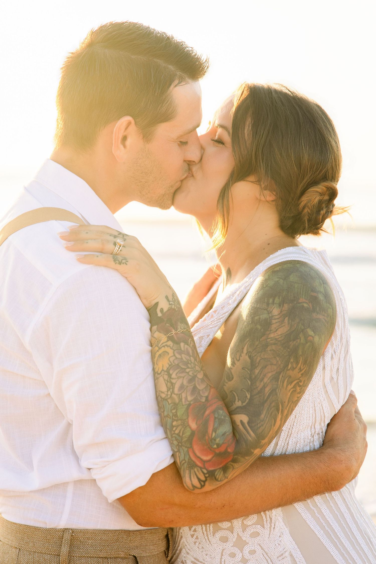 Bride and groom share a kiss bathed in warm golden sunset light on the beach.