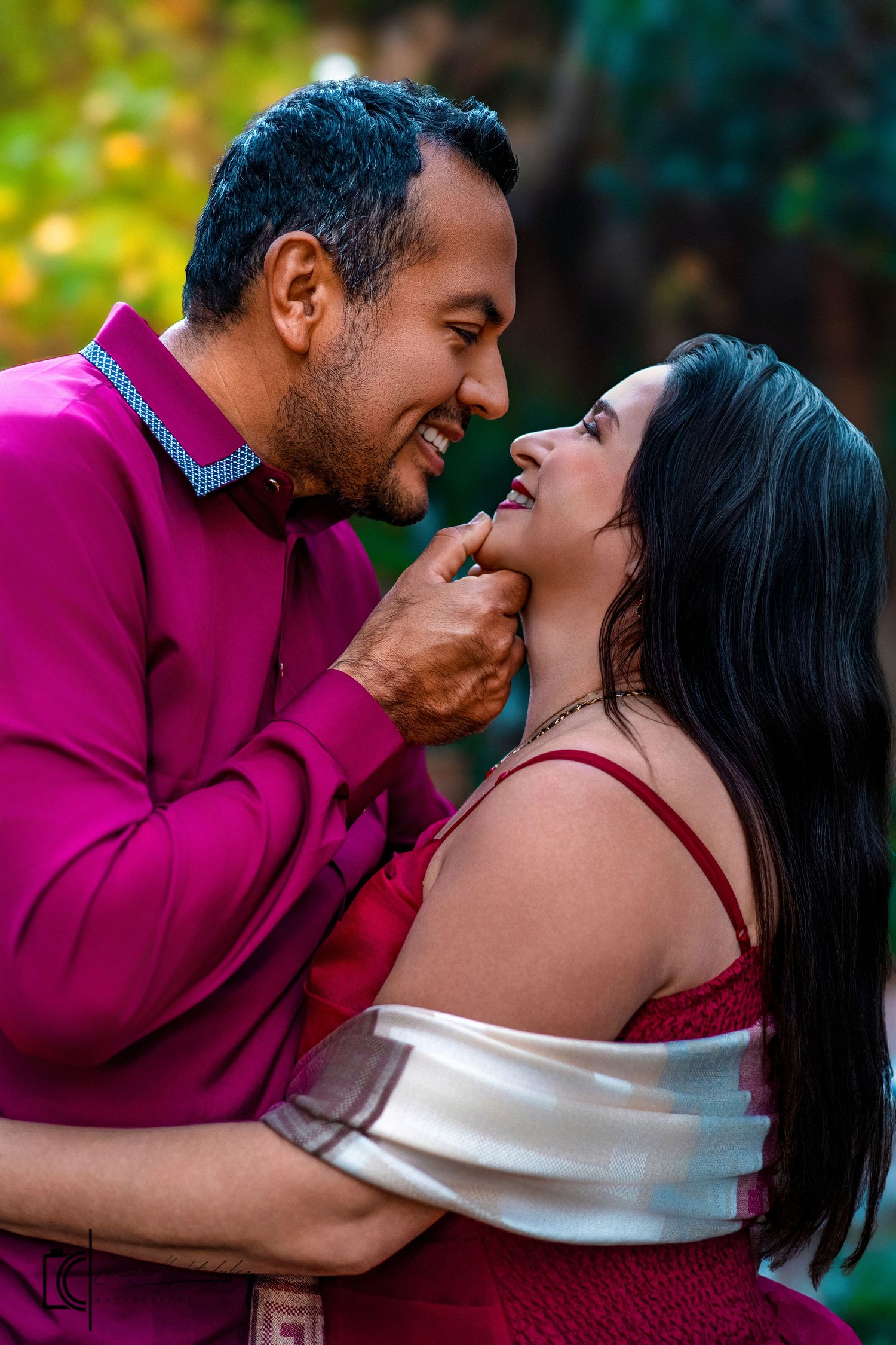 A romantic couple in burgundy attire share intimate kisses during an outdoor photo session.