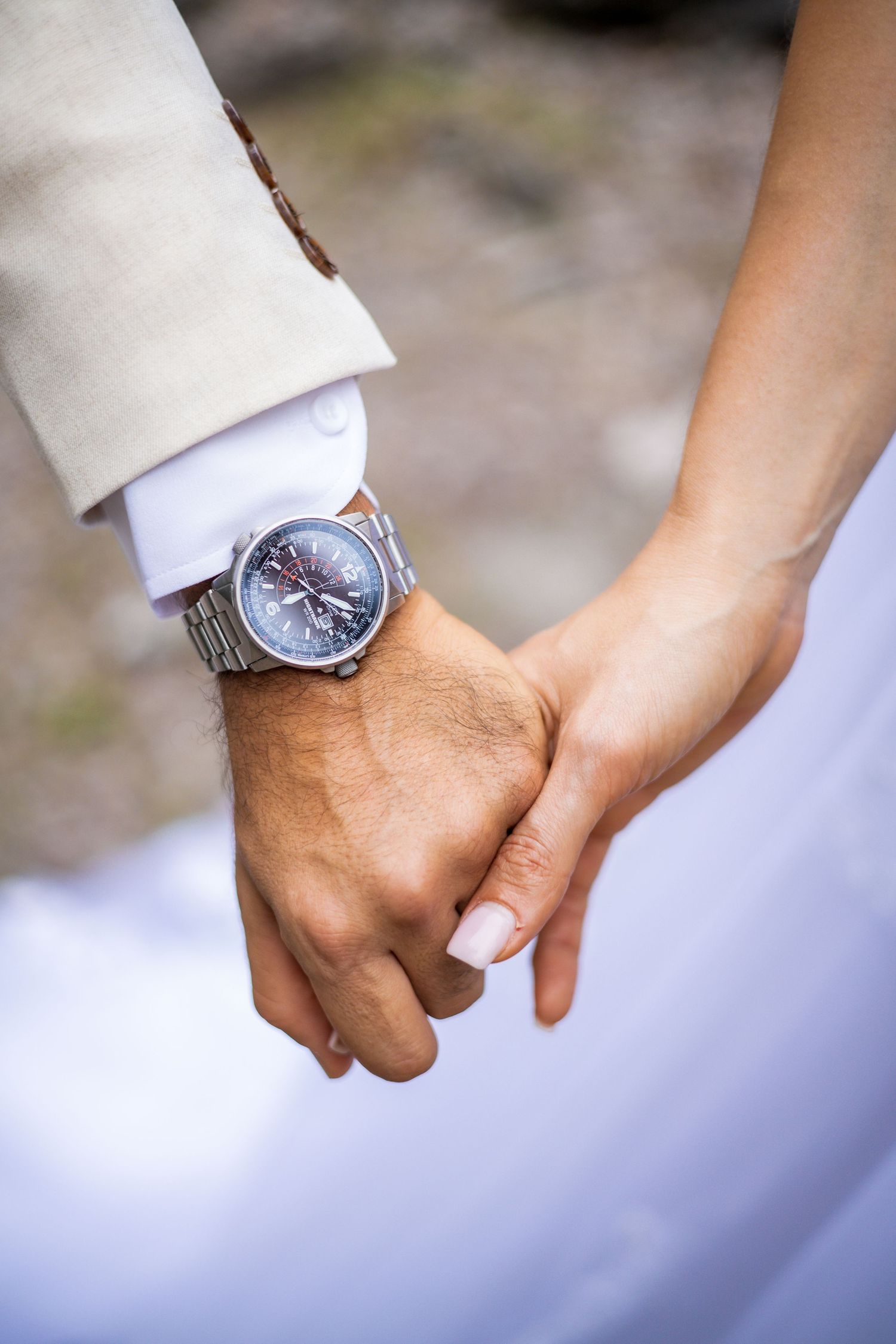 Close-up of hands with wristwatch showing tender moment between couple in wedding attire.