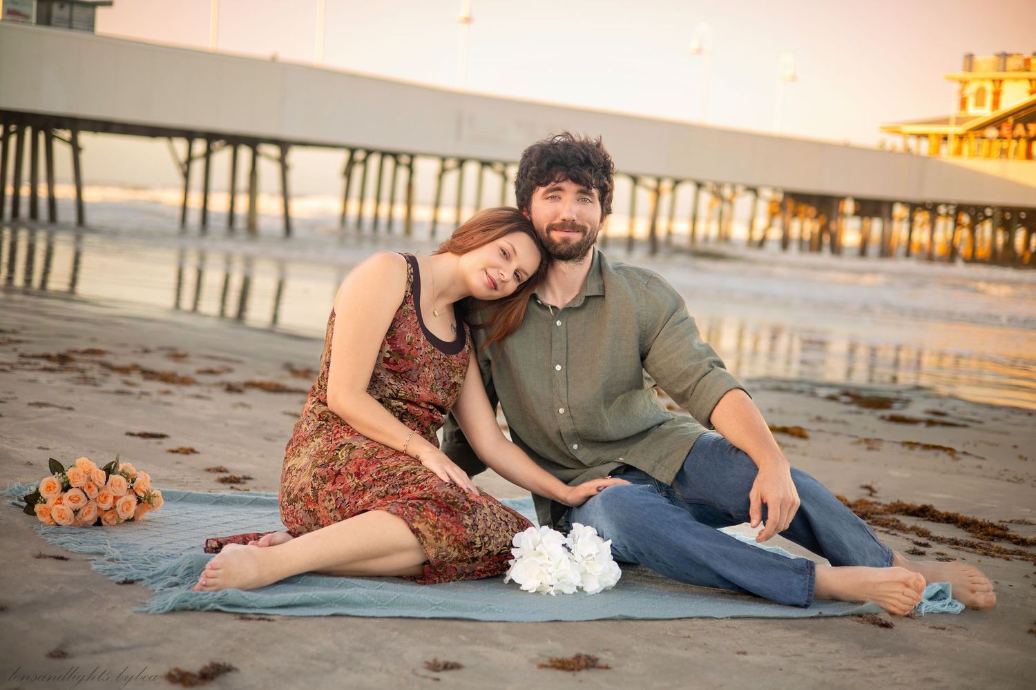Couple relaxing on blanket by pier during sunset beach photography session.